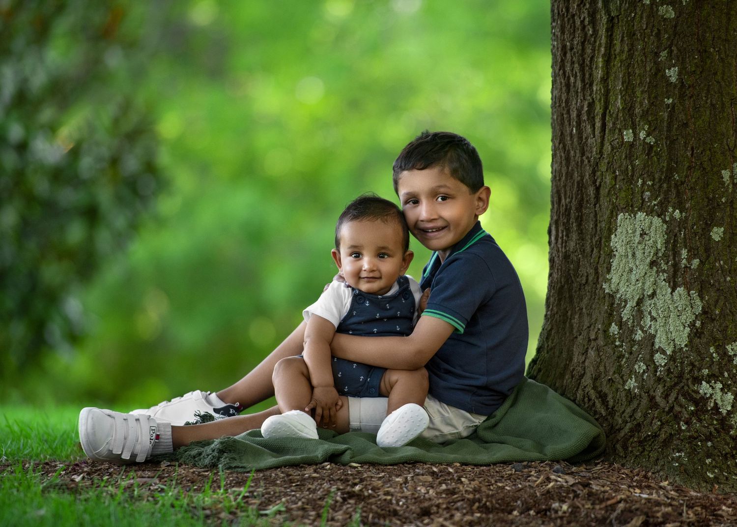 Two children sit together under a shady tree on a bright summer day, sharing laughter and smiles in nature.