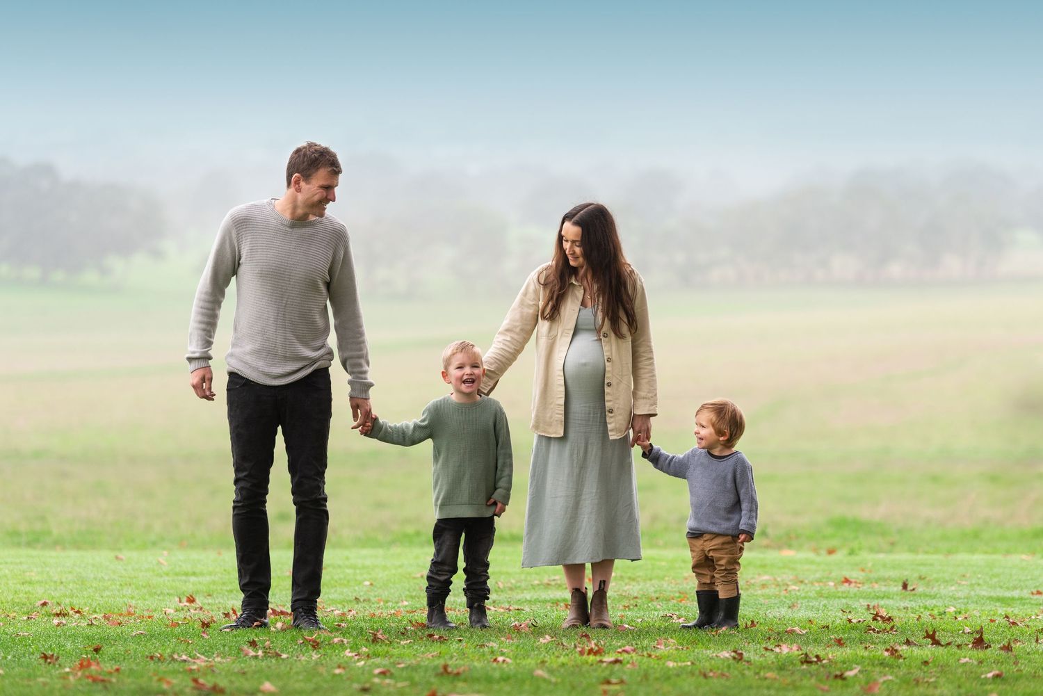 Family walking together holding hands in misty field at sunset.