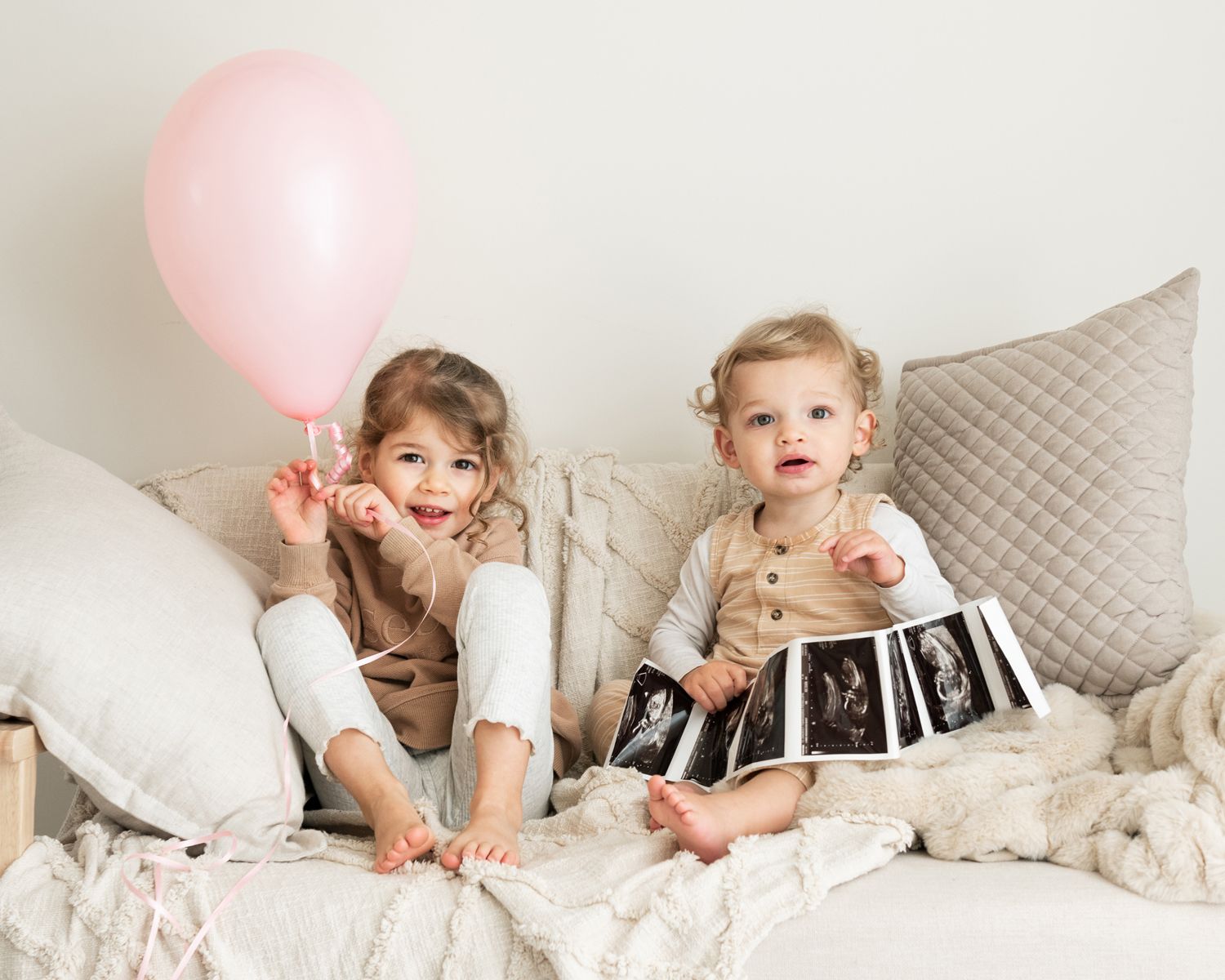 Children playing with pink balloons on white bedding in lifestyle photo session.
