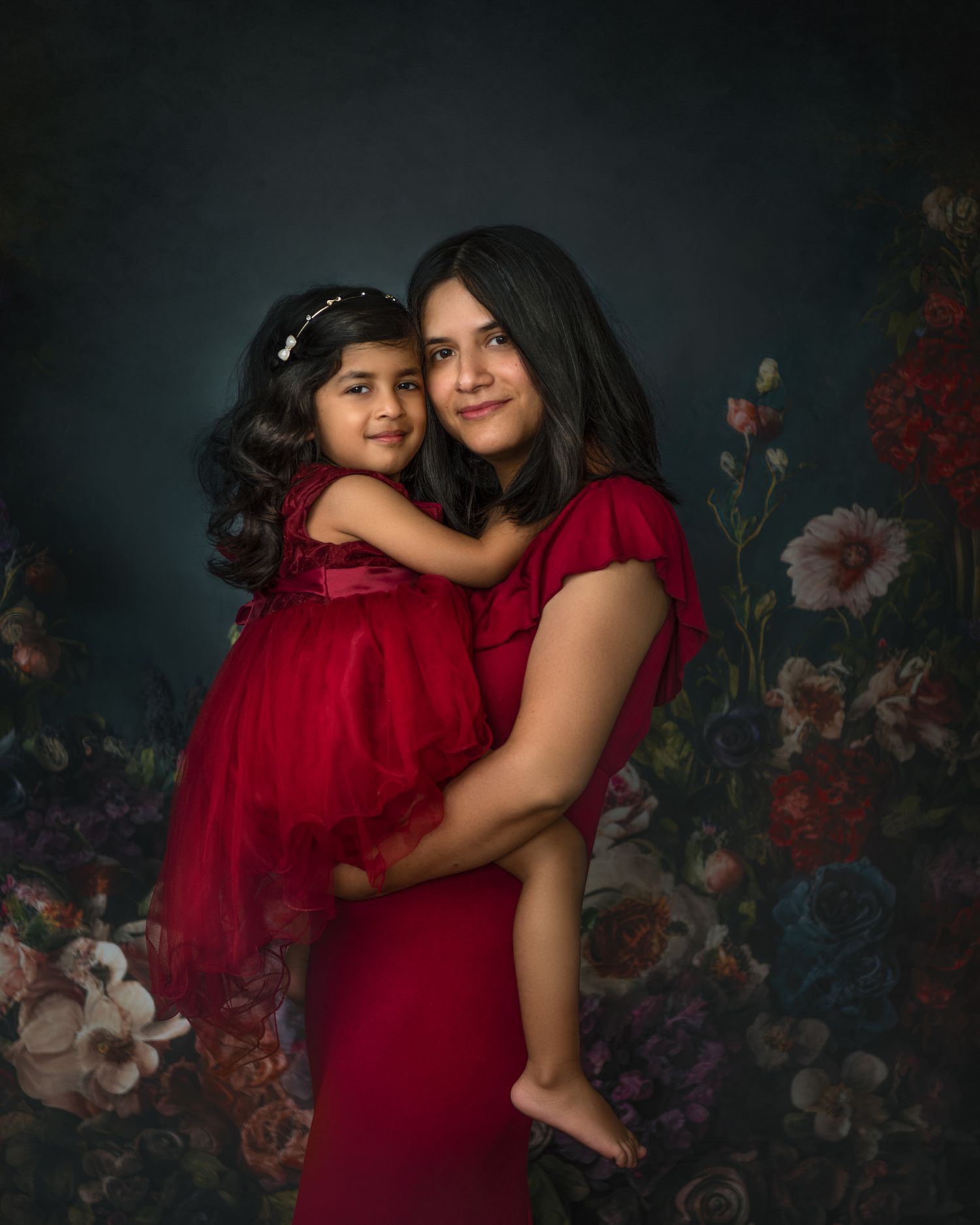 Emotional portraits in matching red dresses against a moody floral backdrop.