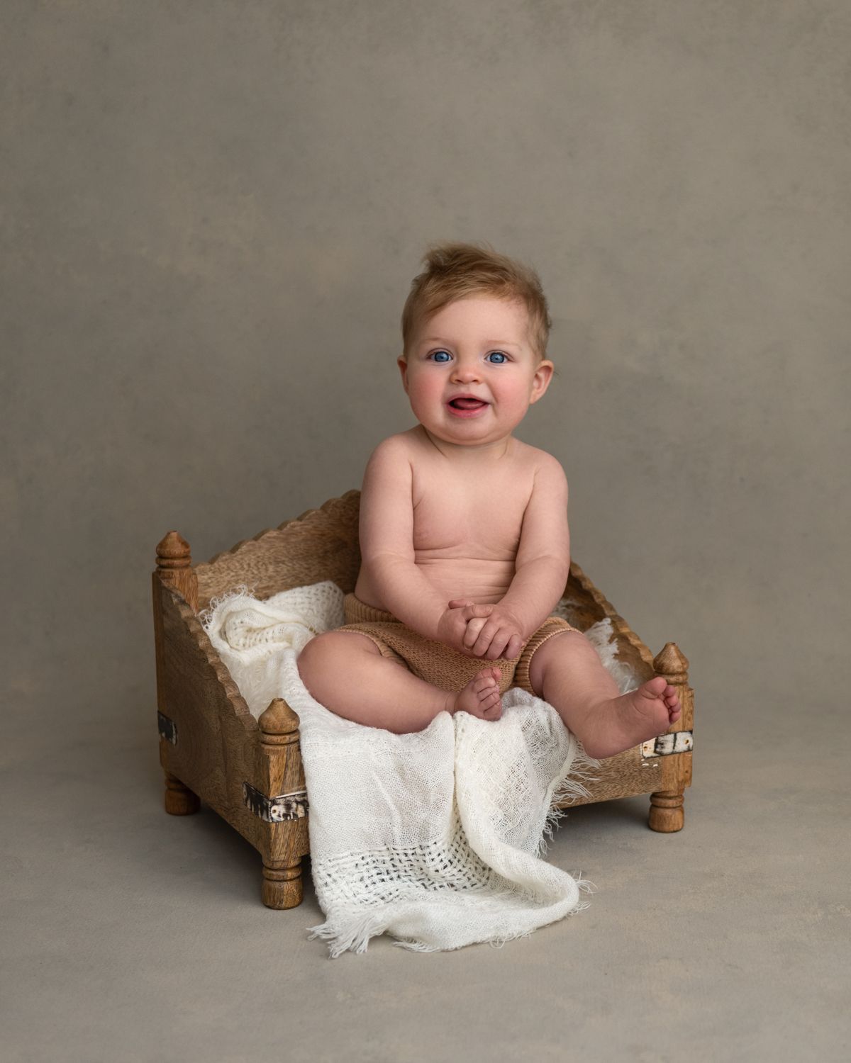 Studio portrait featuring small wooden bench and white lace blanket details.