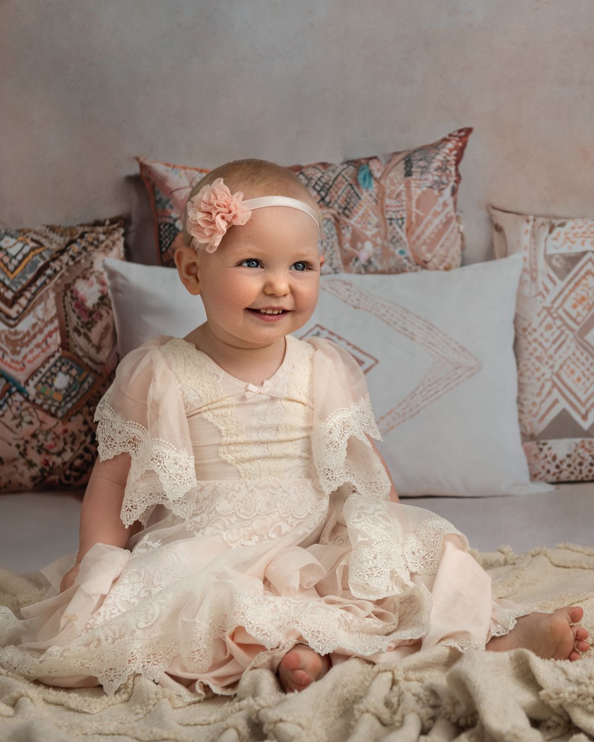 Elegant lace dress and soft pillows create romantic setting against neutral background.