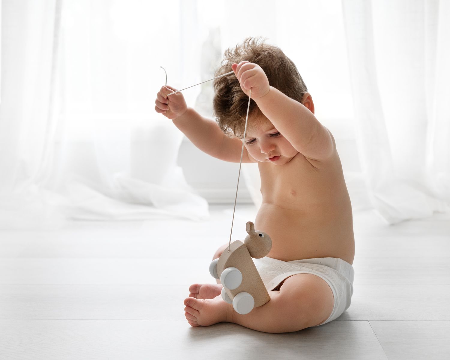 Baby in white diaper crawls on bright white background.