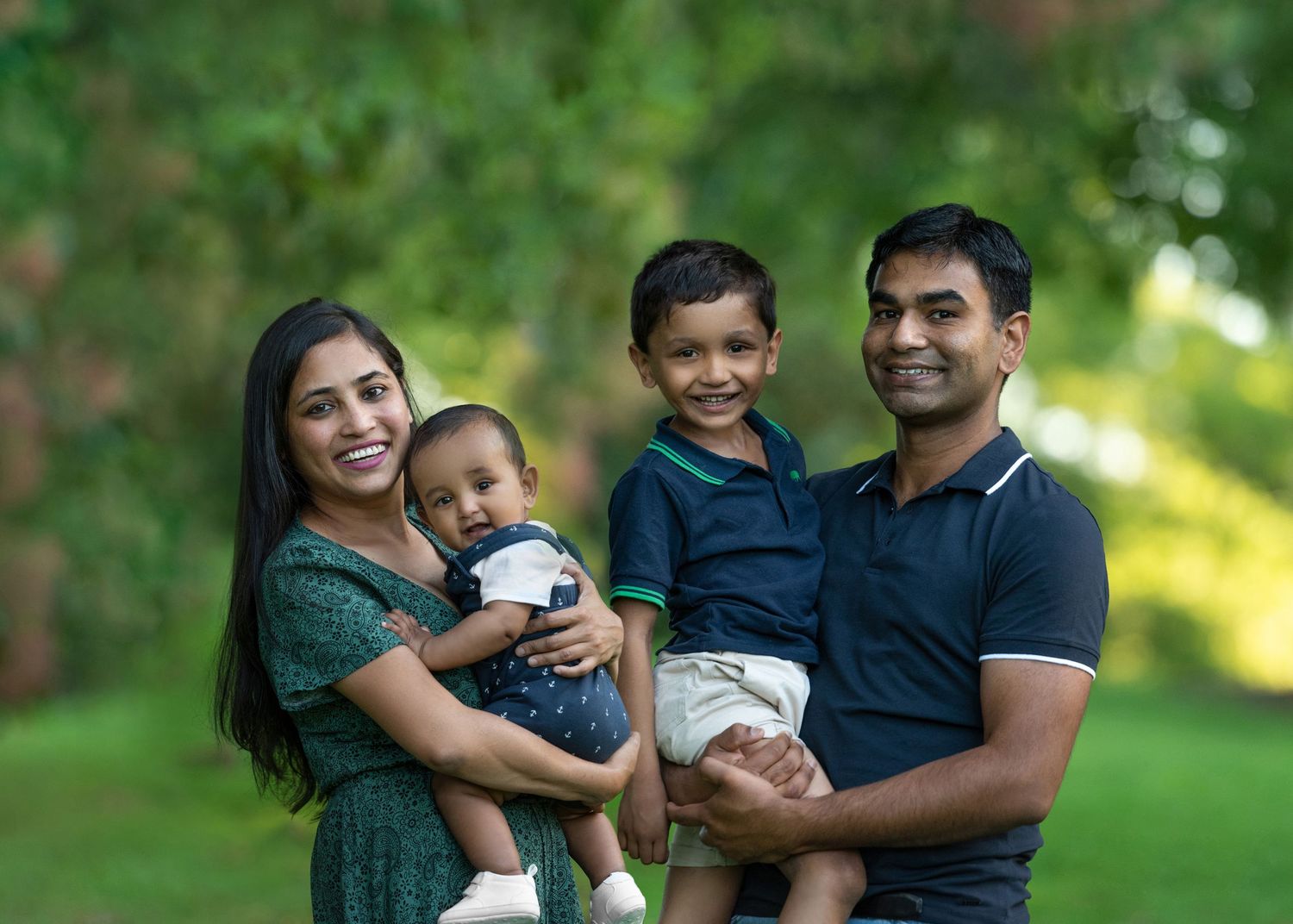 A happy family in matching navy and green outfits poses together outdoors for a series of casual portraits.
