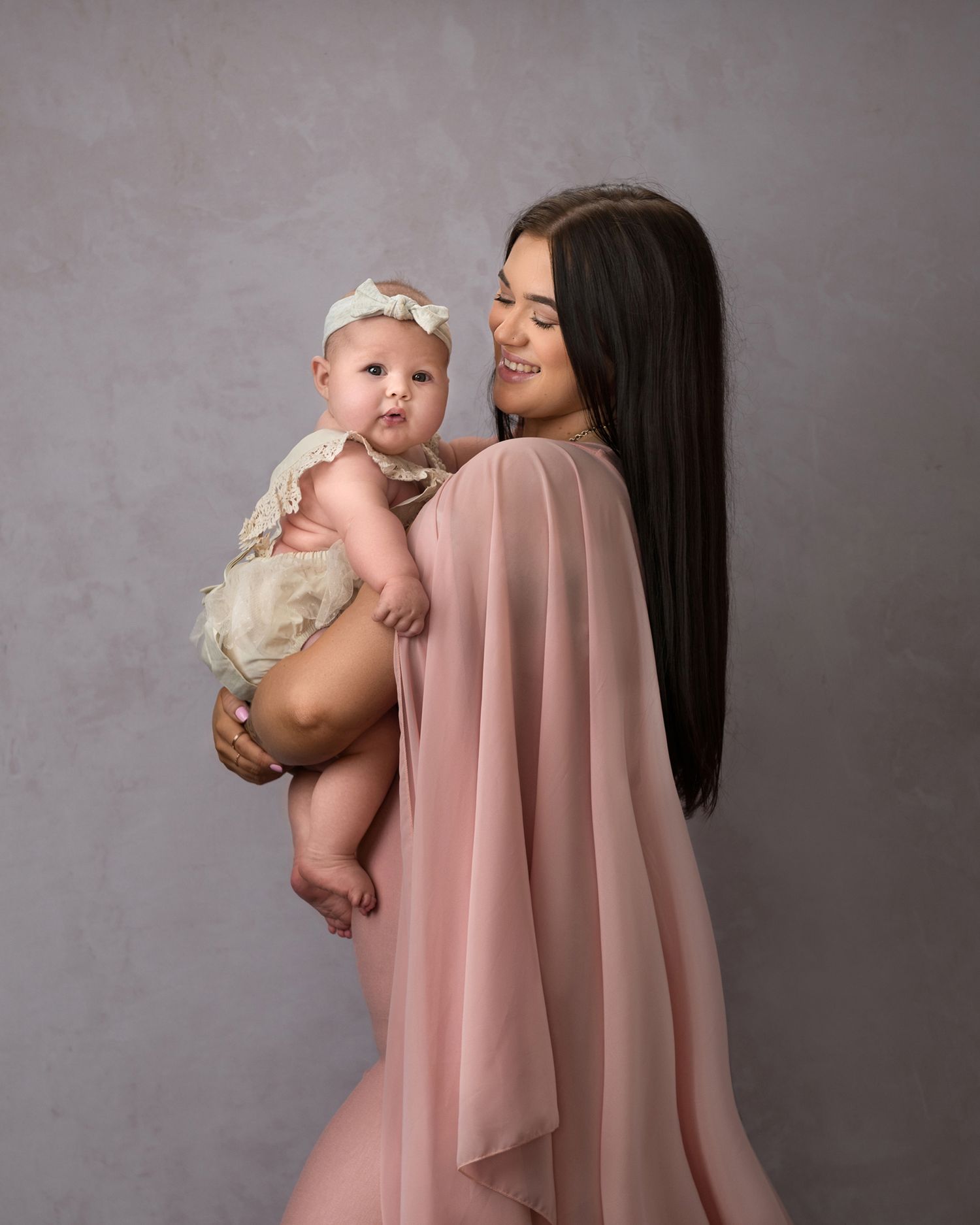 A tender moment captured in a studio portrait featuring a pink flowing dress against a grey backdrop.