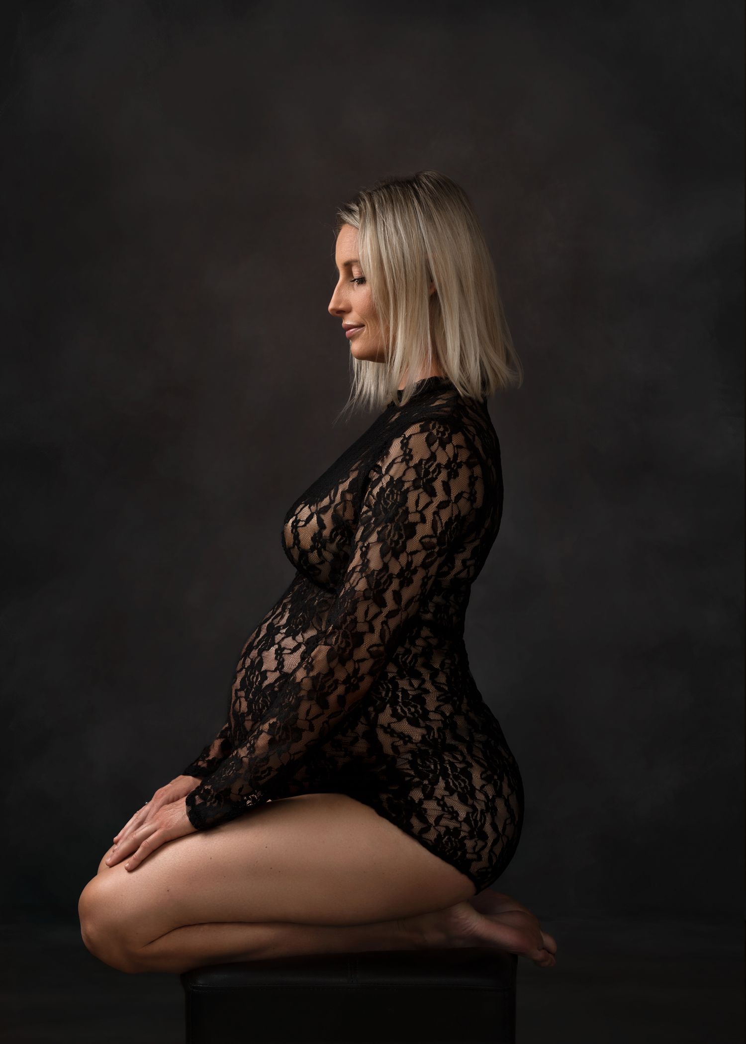 Artistic maternity portrait featuring black lace against dark background.