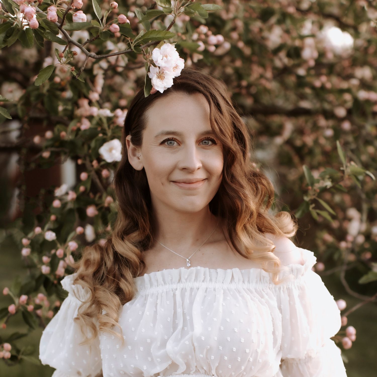 Portrait in a dreamy spring garden with blooming cherry blossoms and soft white lace dress details.