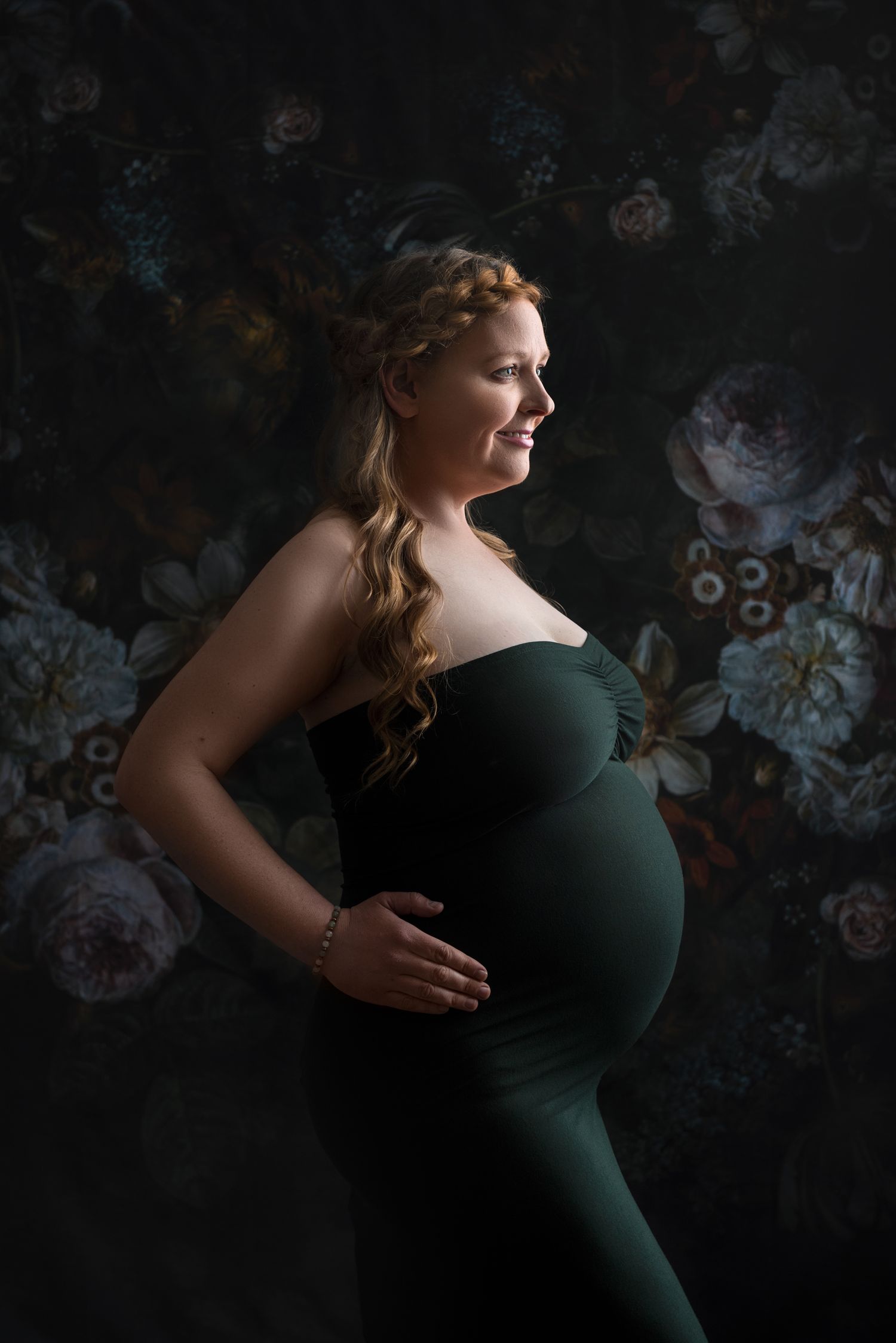 Elegant maternity silhouette in green dress against floral backdrop.