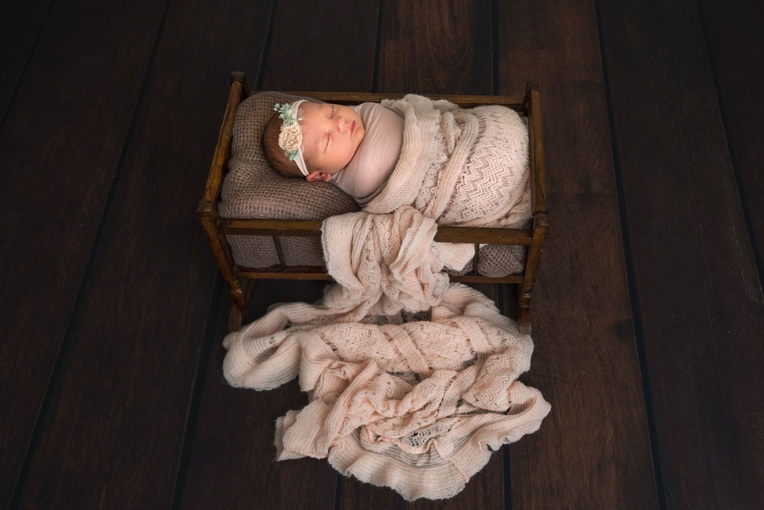 Newborn baby wrapped in beige fabric lying on wooden prop bed.