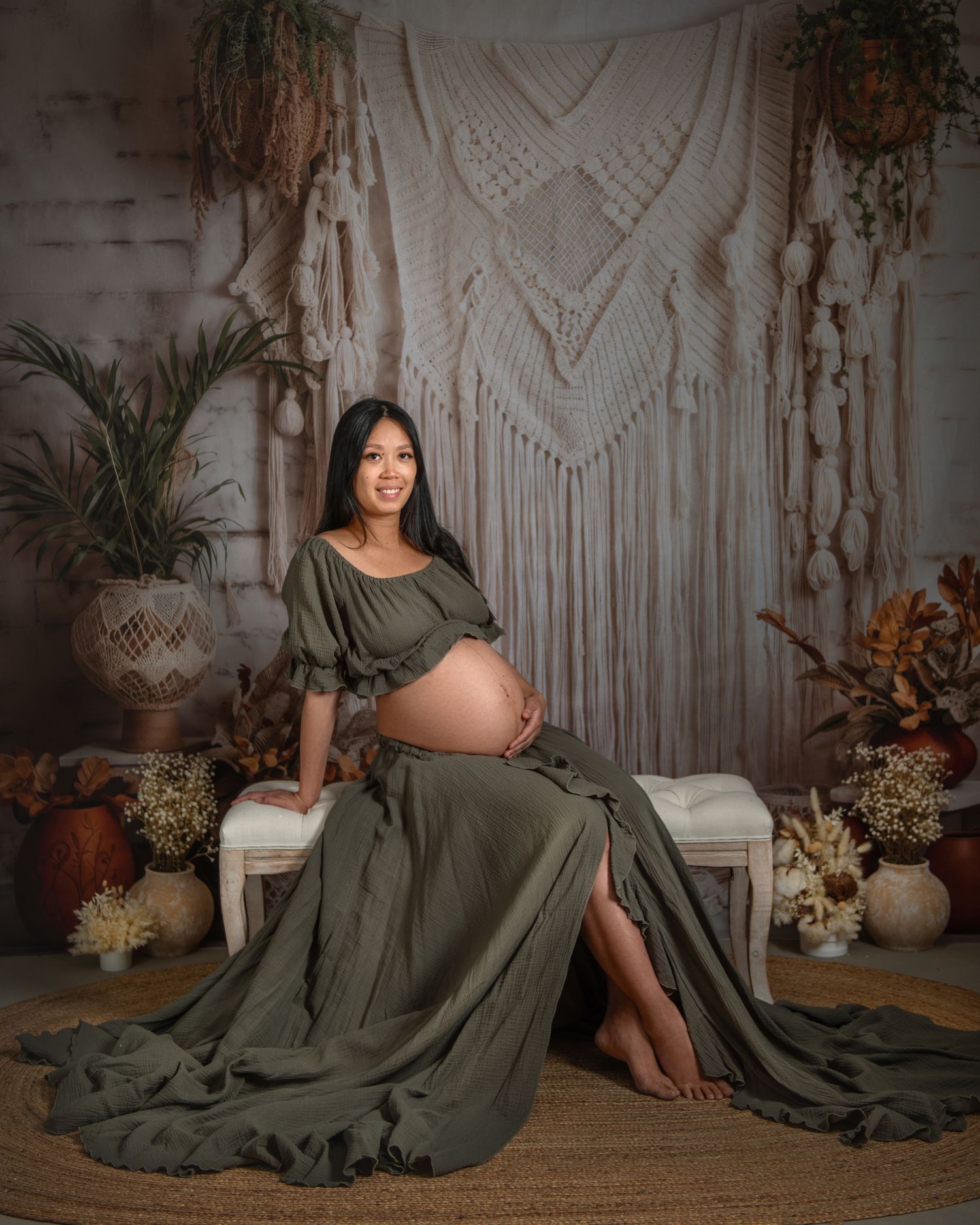 Boho maternity session with olive green dress against macrame backdrop and dried flowers.