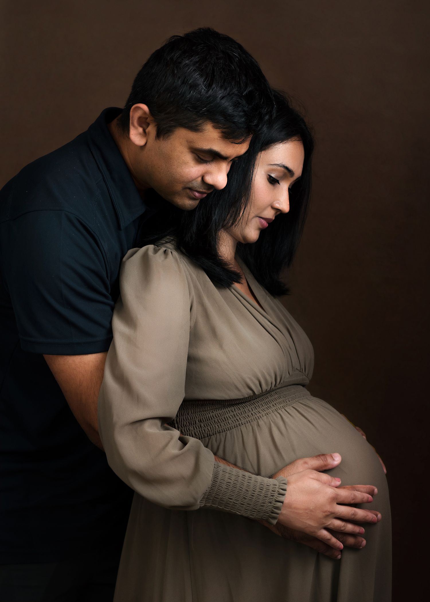 Intimate maternity portrait of couple in dark studio setting with dramatic lighting.