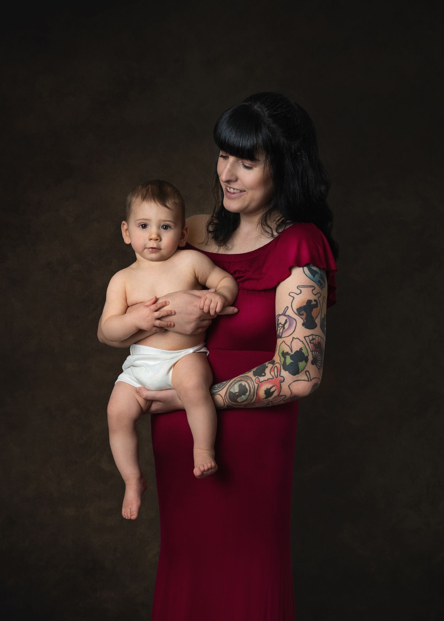 Studio portraits featuring a burgundy dress and artistic tattoos against a dark background.