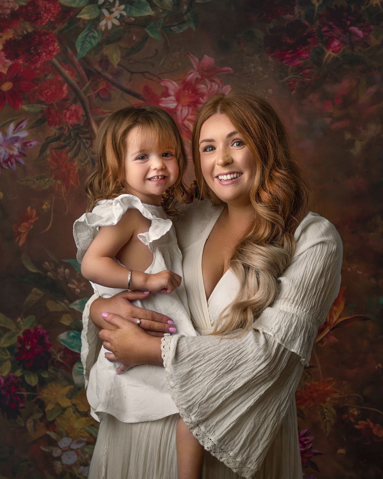 Studio portraits with white dresses against a romantic floral backdrop with deep red blooms.