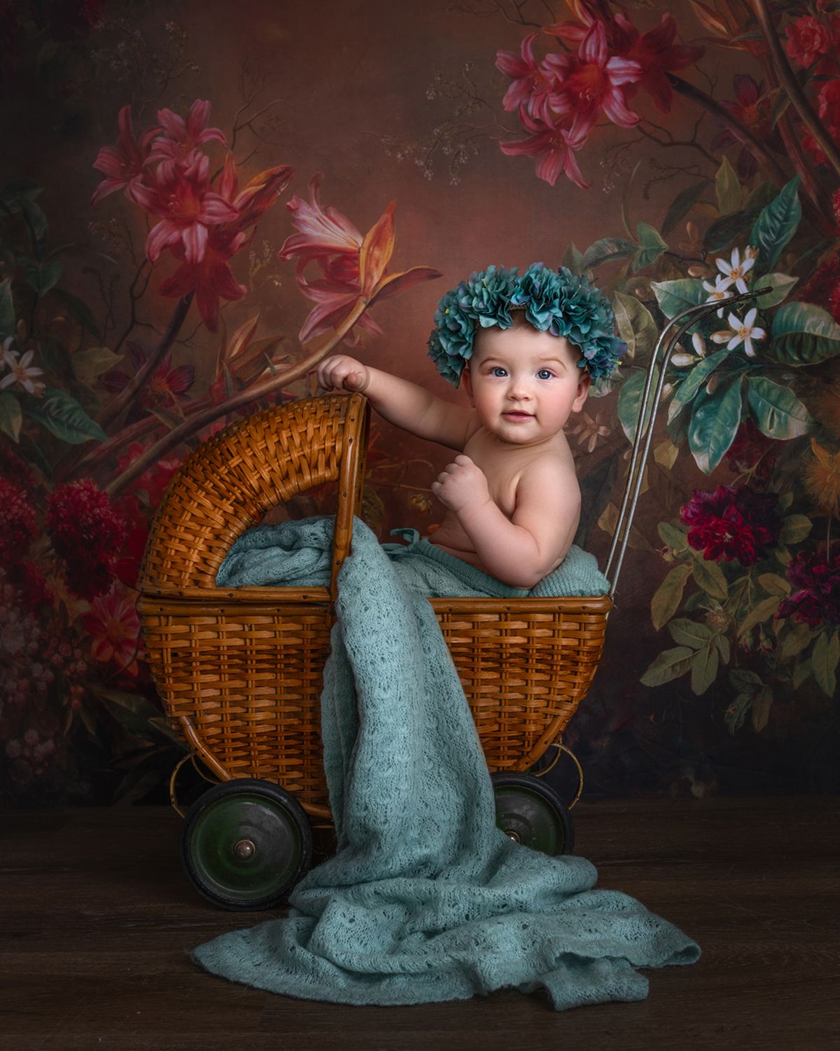 Artistic baby photography setup with wicker basket and turquoise accessories against dark floral background.