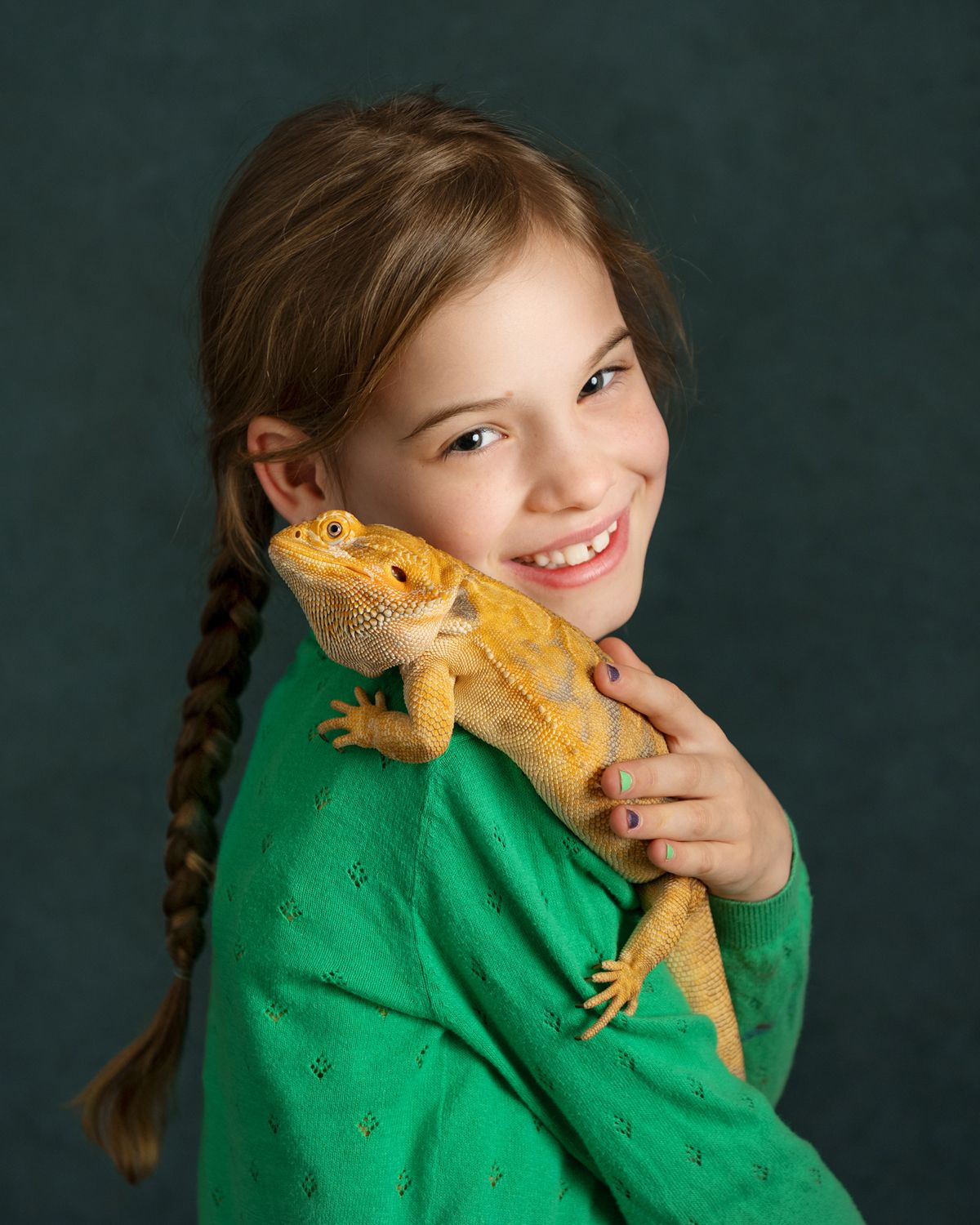 Child in green sweater playfully poses with yellow bearded dragon lizard.