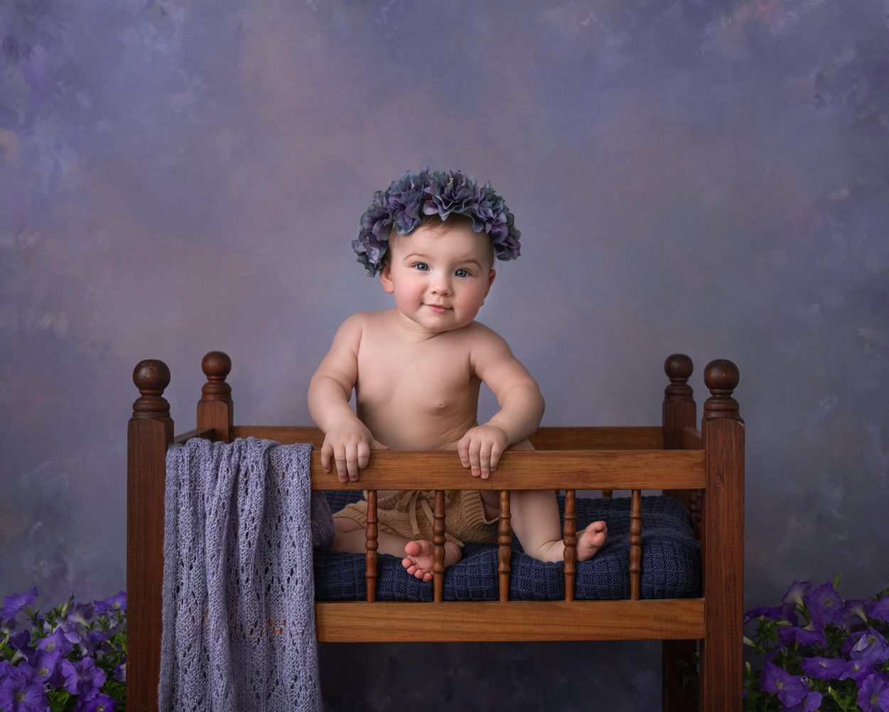 A wooden headboard with gray fabric draped over it and purple flowers visible in the background.