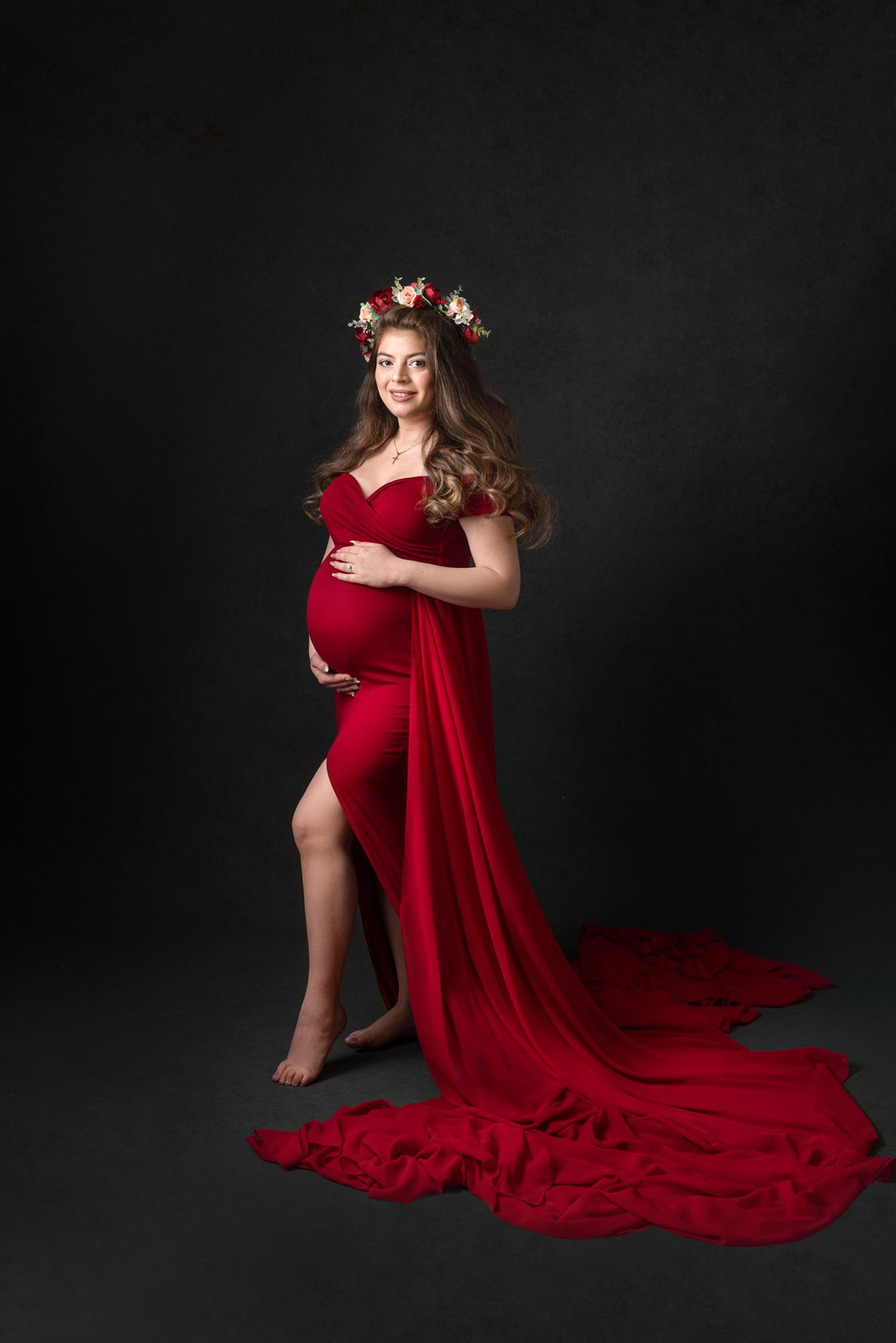 Elegant maternity portrait with dramatic red flowing dress on black backdrop.