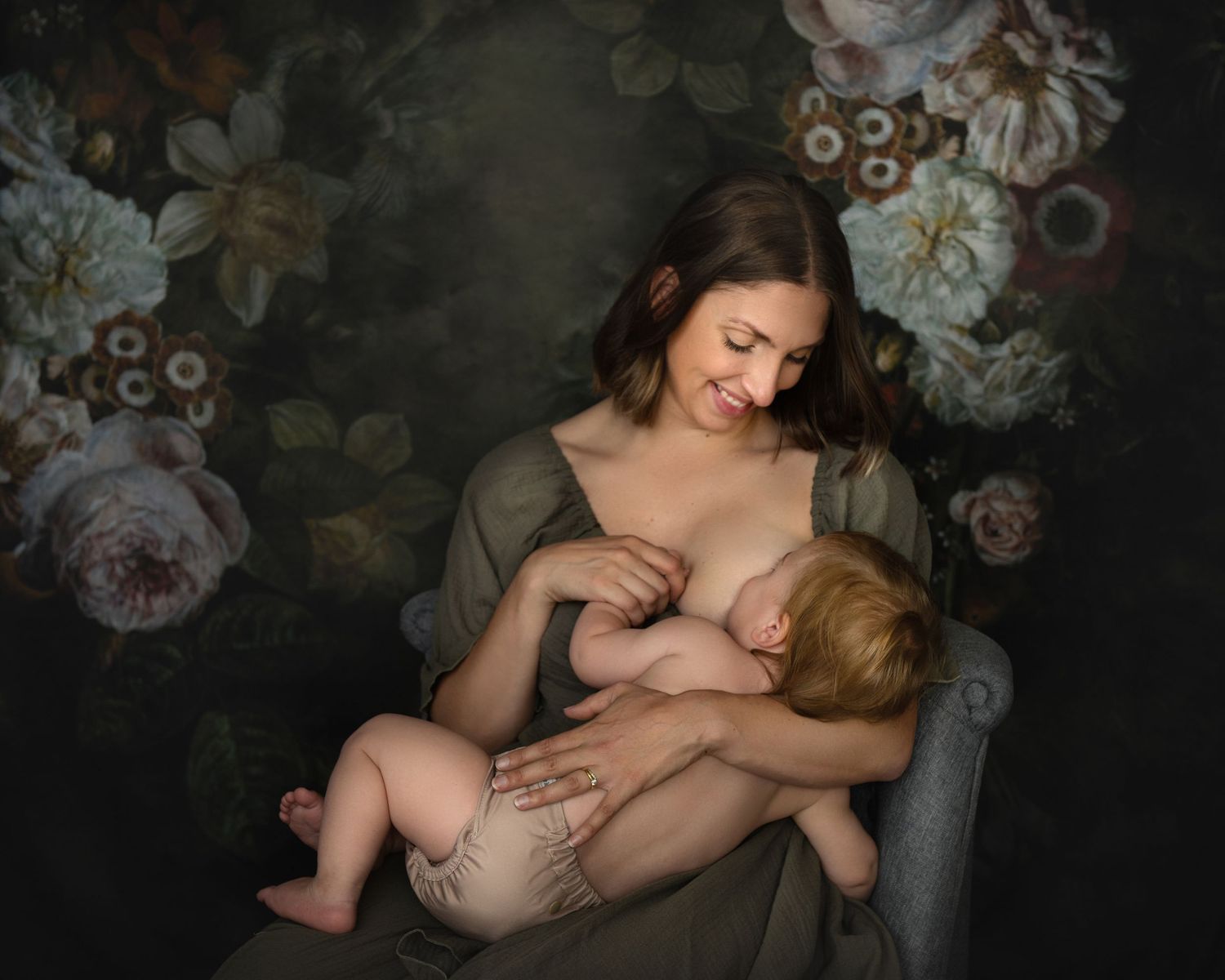 Artistic maternity portraits with floral backdrop in moody lighting.