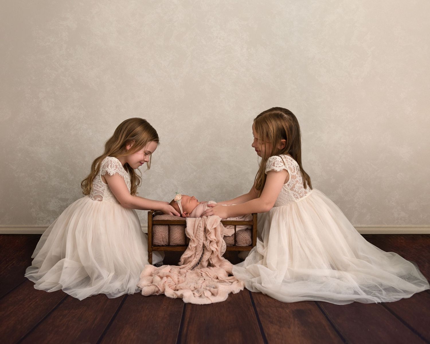 Two children in white dresses lay on wooden floor mirroring each other's poses.