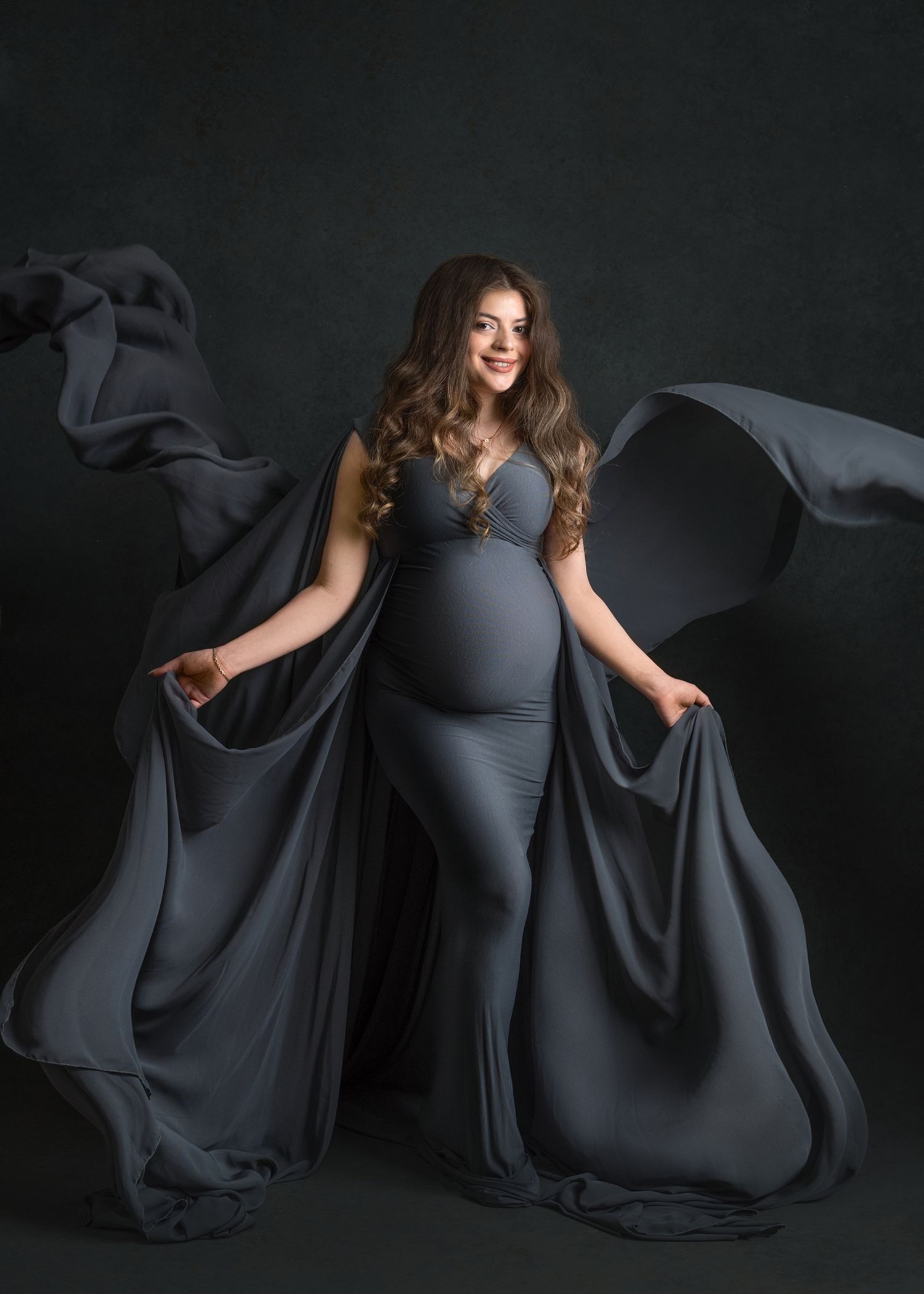 A maternity portrait featuring flowing gray fabric against a dark background.