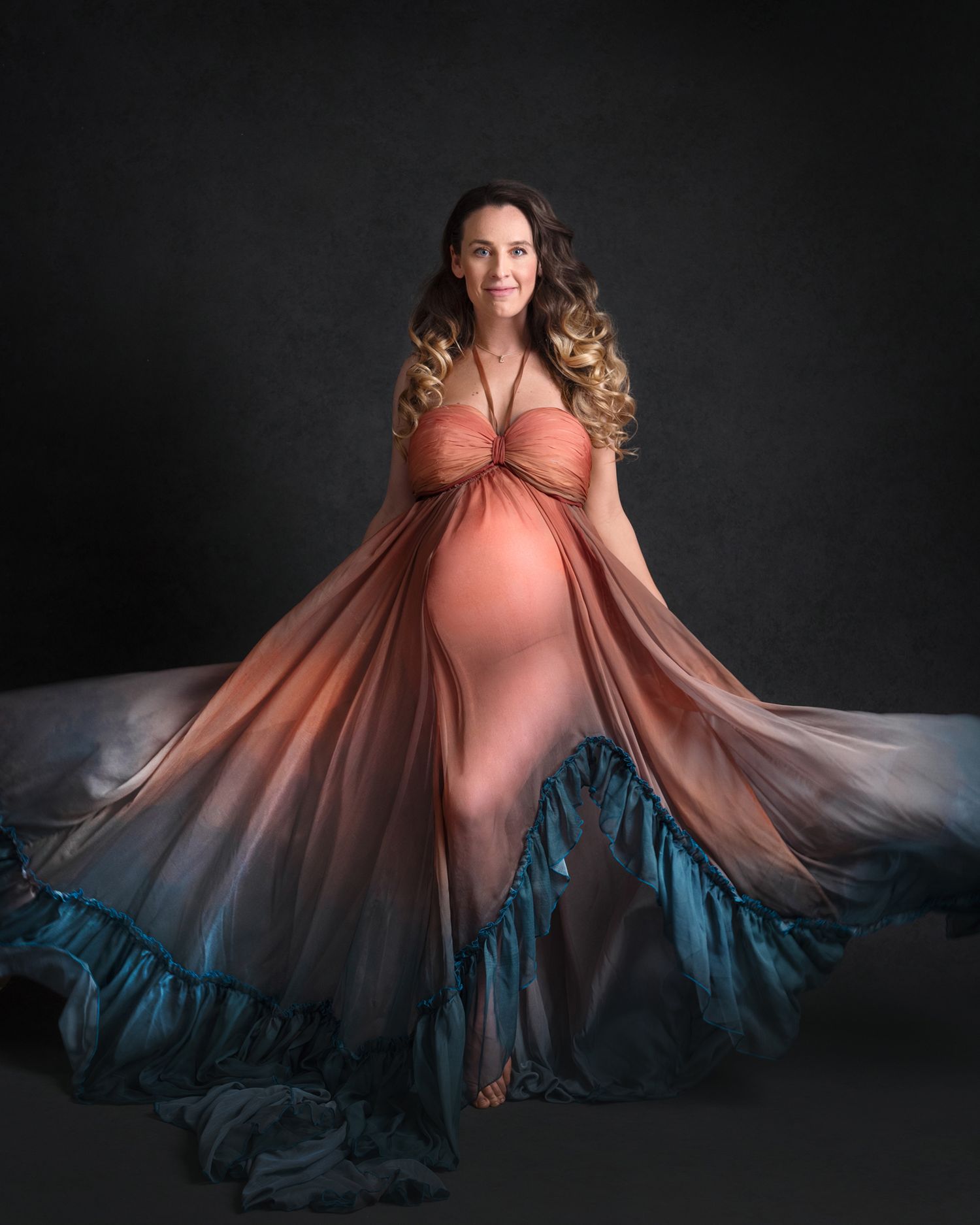 Flowing coral ombre dress creates dramatic movement in maternity portrait.