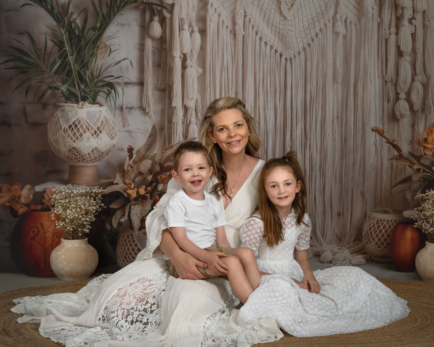 Family portrait session with white lace dresses against a macrame backdrop with boho decor and pumpkins.
