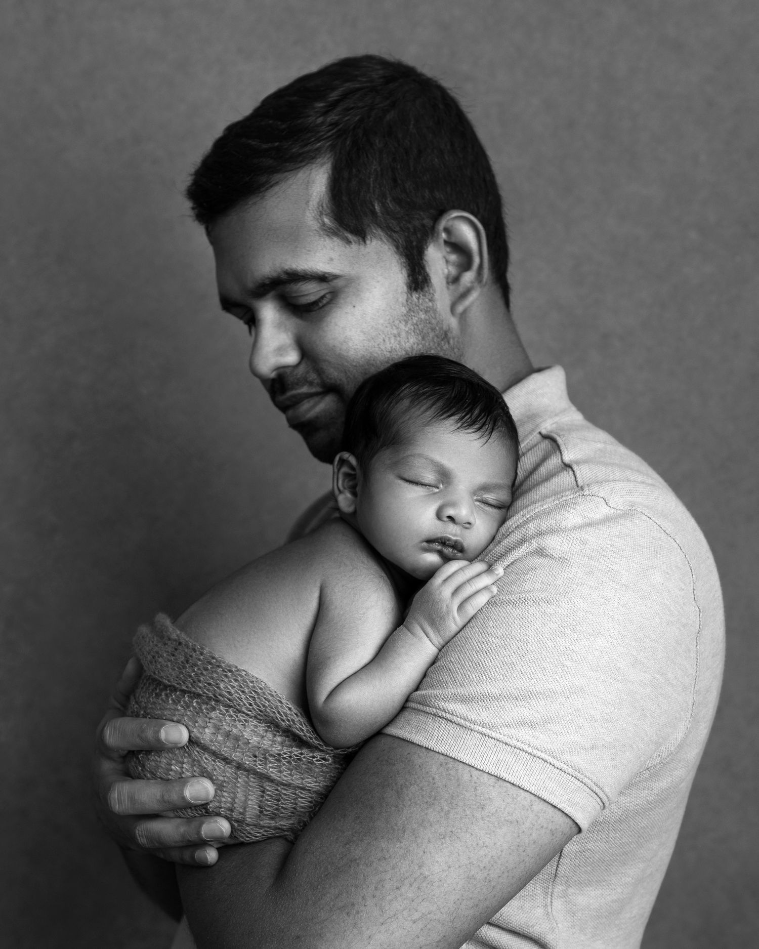 Black and white portrait showing tender moment between parent and sleeping baby.
