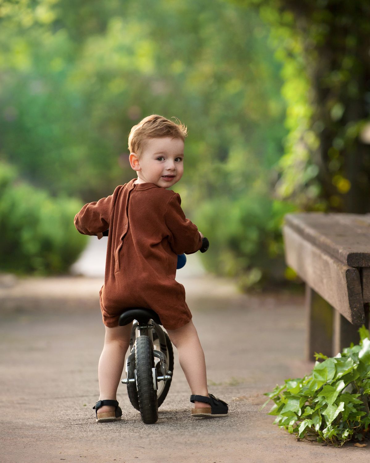 Small child riding tricycle on outdoor path in brown clothing.