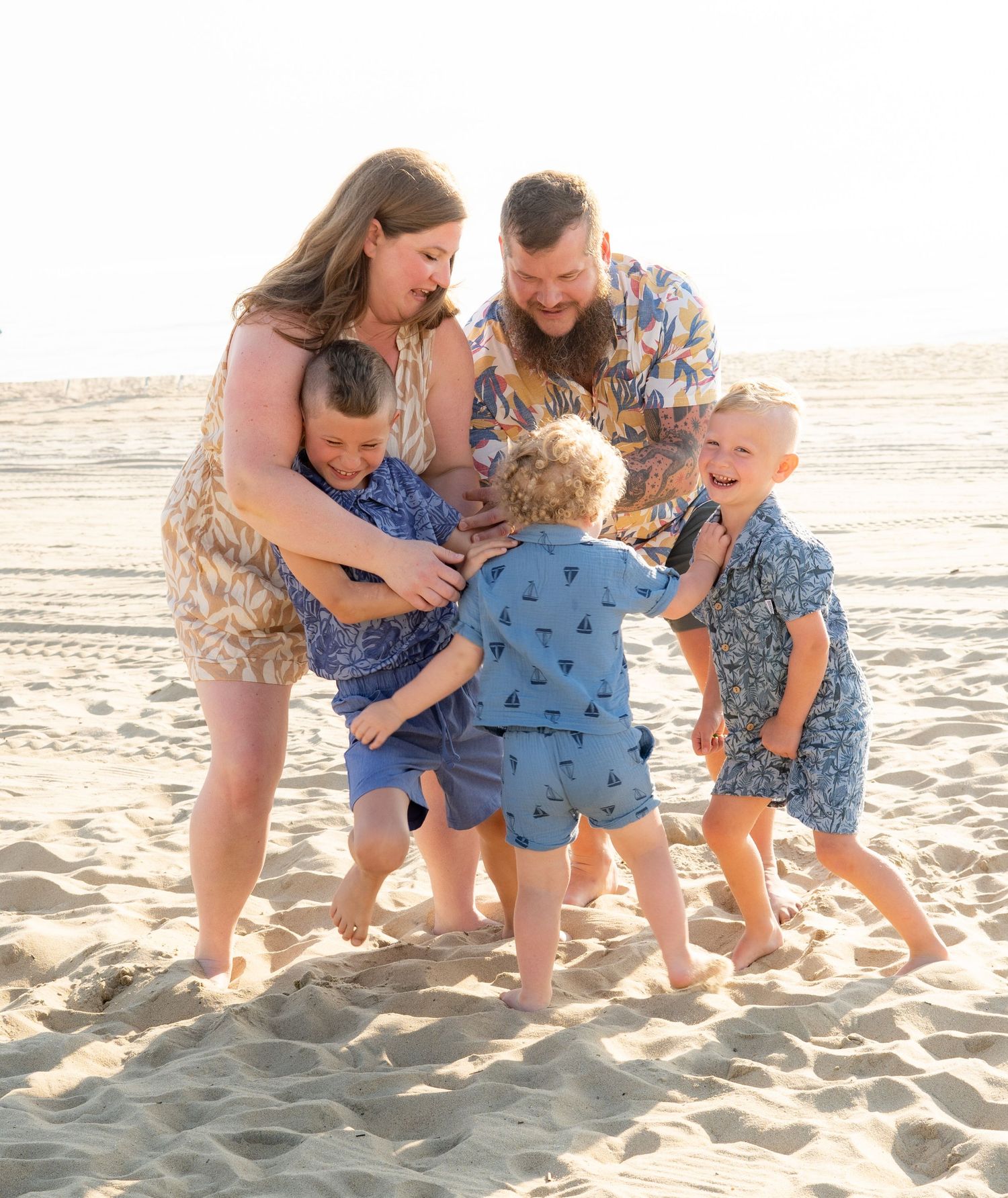 A family in coordinated blue outfits plays together on a sunny beach during golden hour.