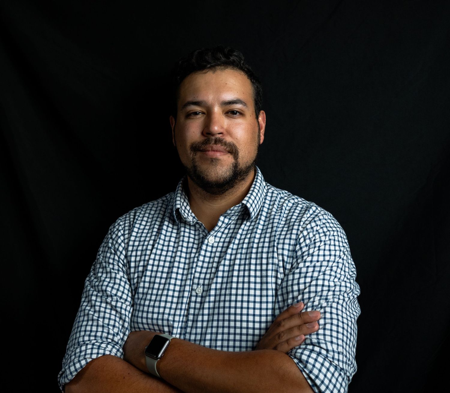 Professional headshot of person in black and white checkered button-down shirt against dark background.