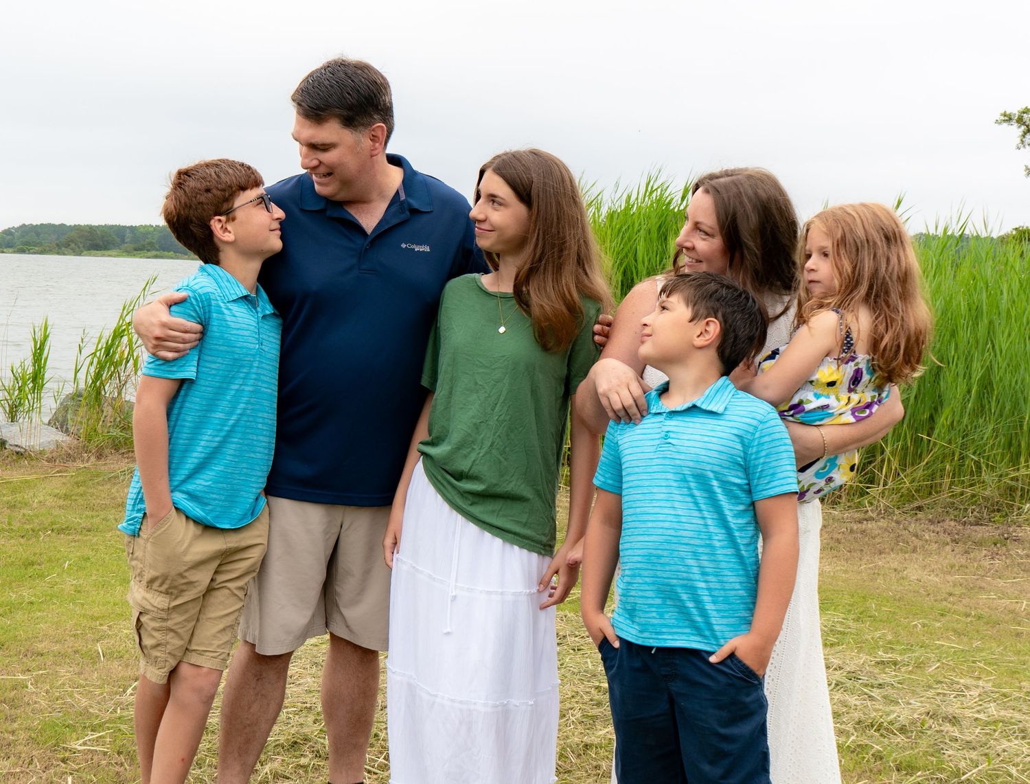 Happy family gathering outdoors on a sunny day by the water wearing coordinated blue and green outfits.