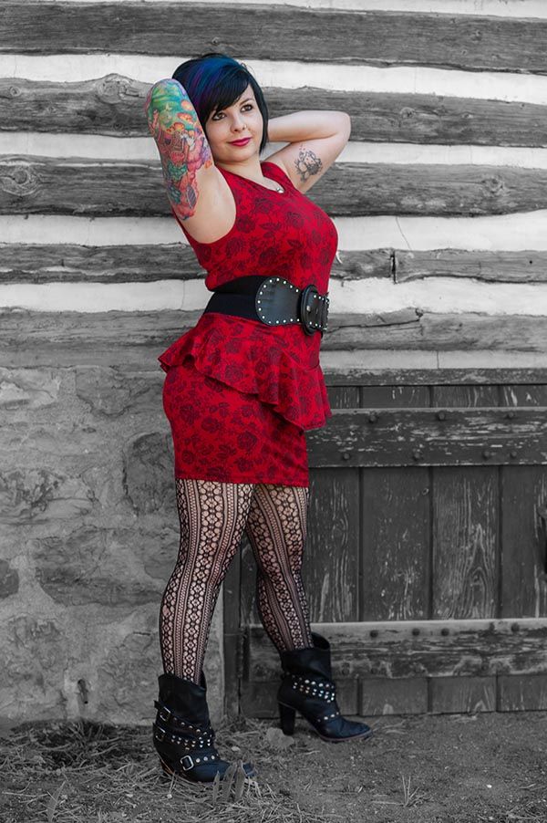 Artistic portrait with red dress and patterned tights against rustic log cabin wall.