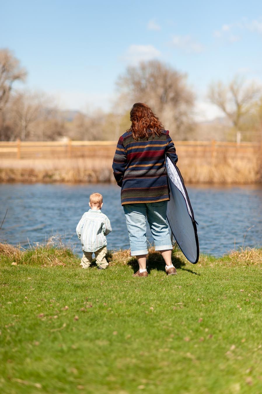People sitting together on grassy bank overlooking a lake on a sunny day.
