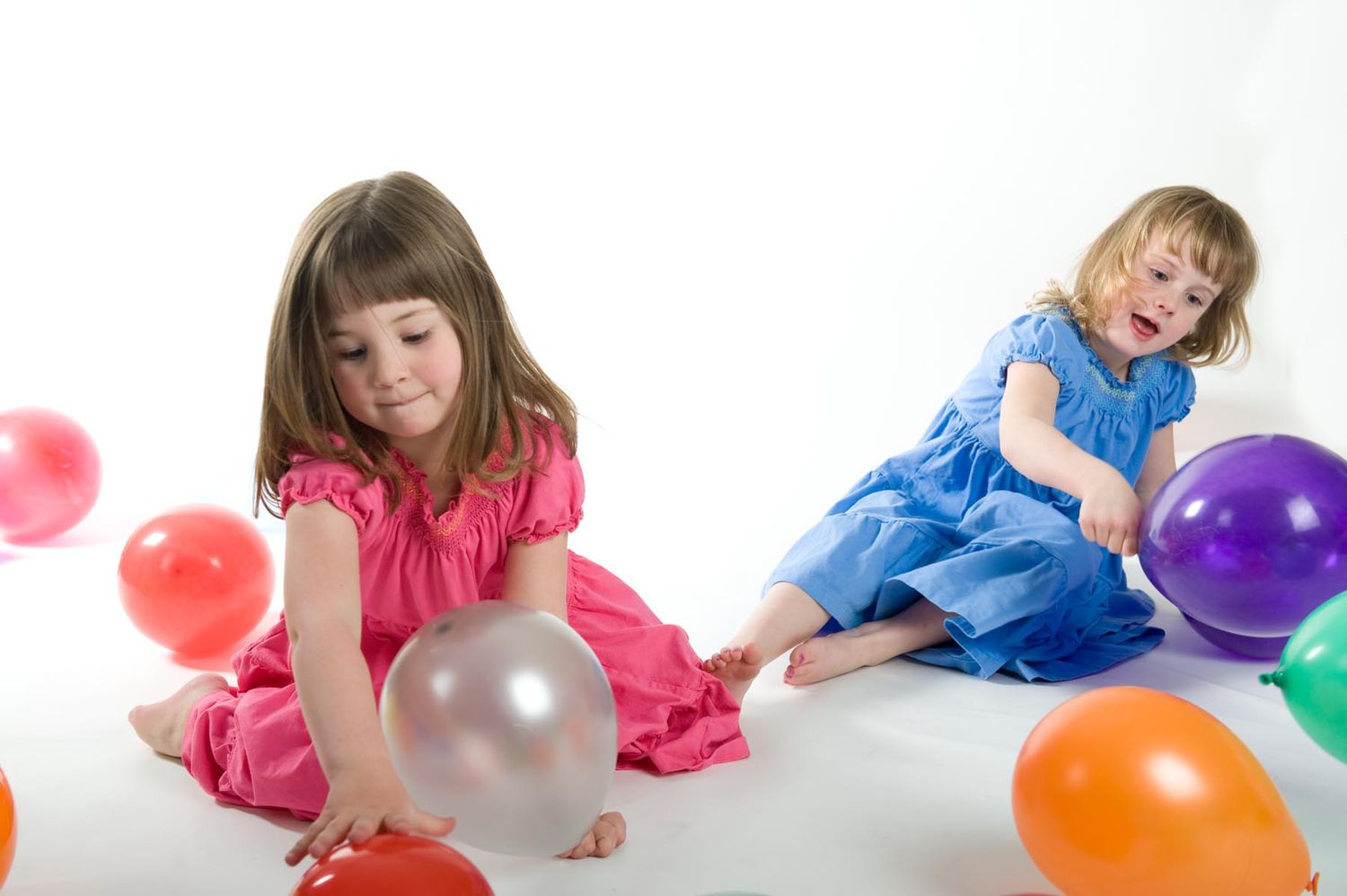 Children in pink and blue outfits play with colorful balloons on a white background.