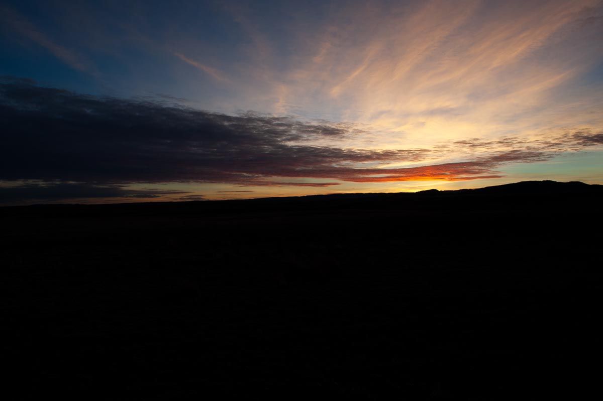 Dramatic sunset panorama with colorful clouds stretching across mountain horizon.