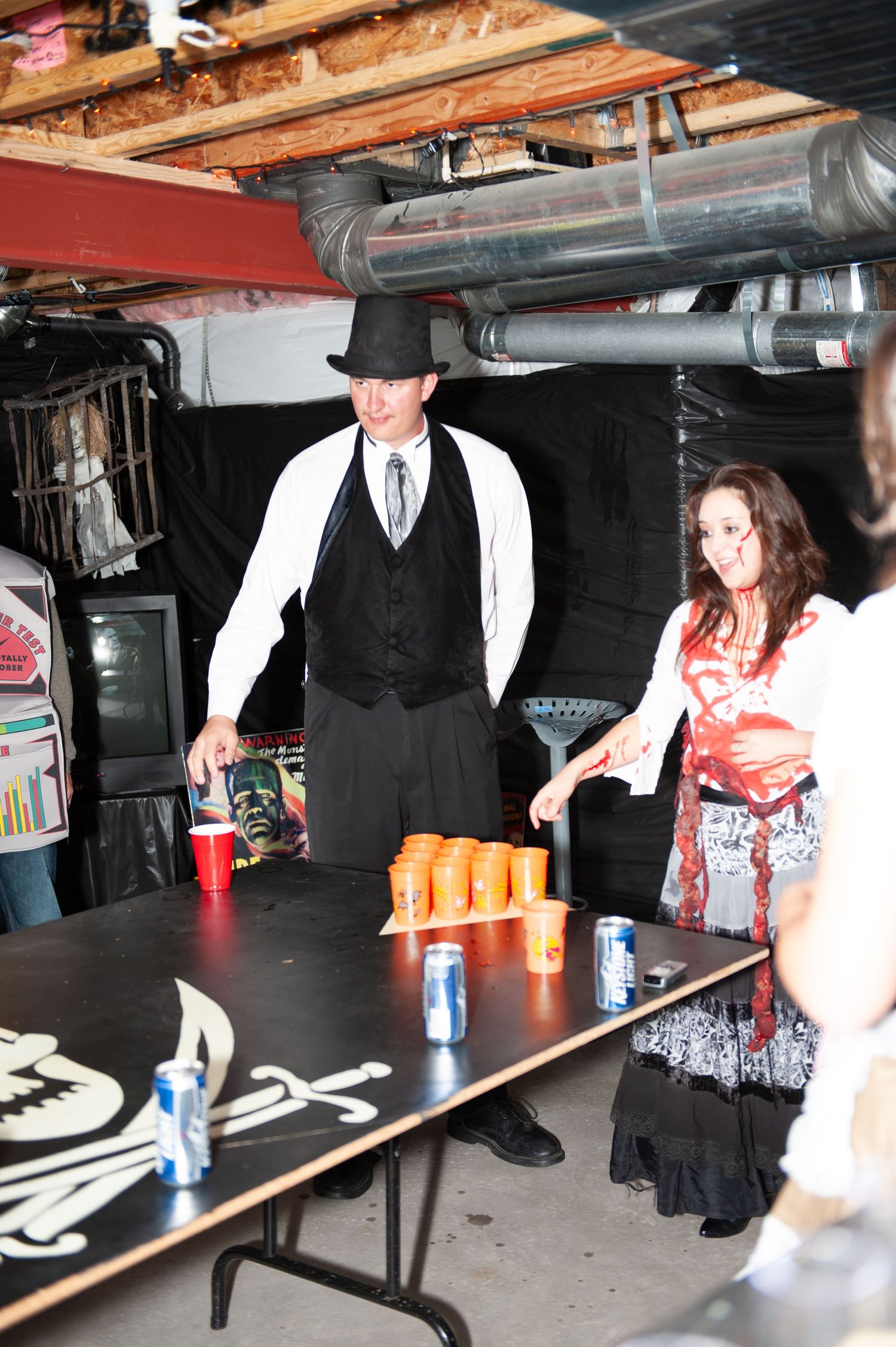 People playing beer pong on a long table in a dimly lit basement setting.