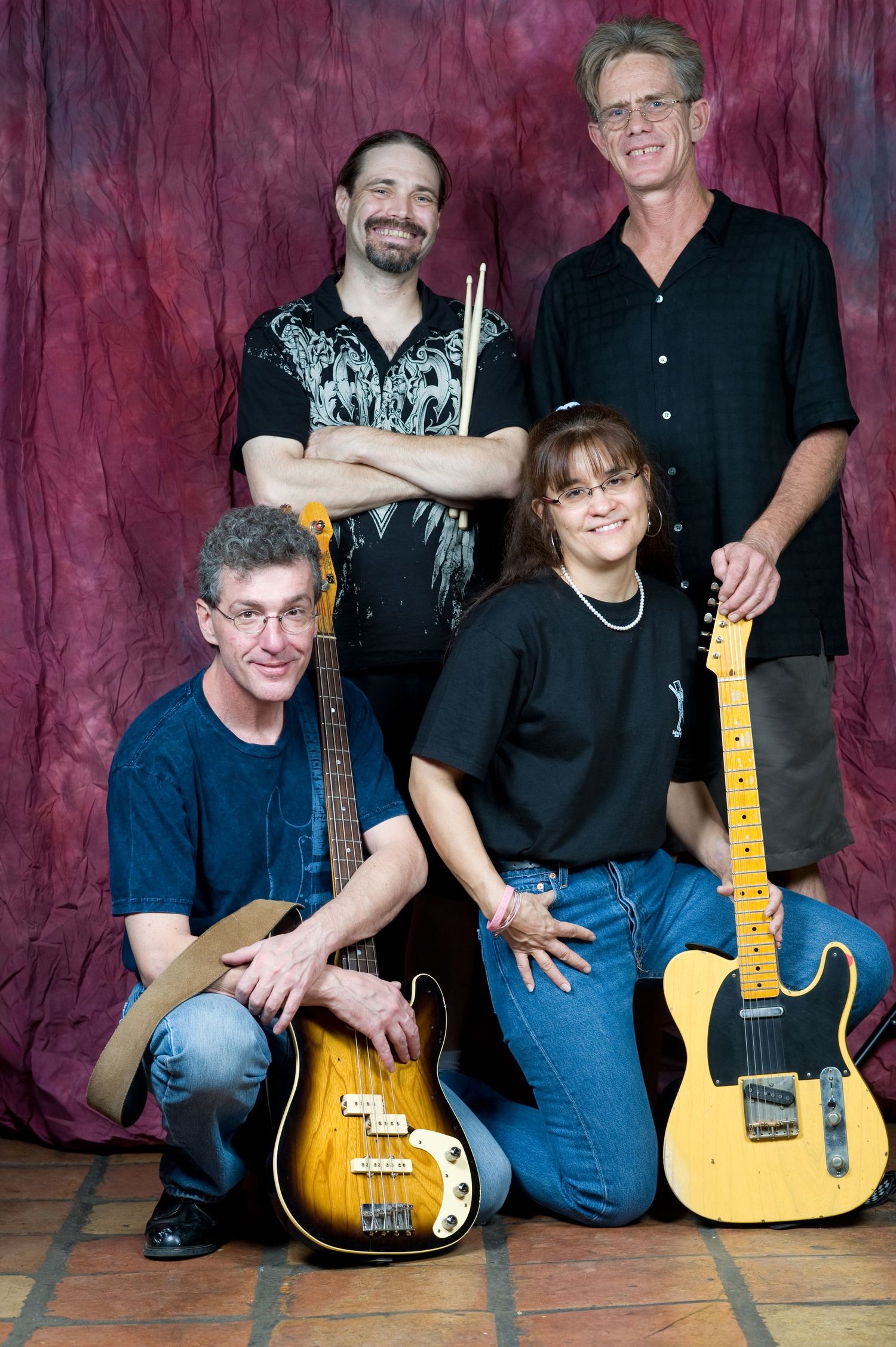 A music band poses with their instruments including a bass guitar and yellow electric guitar against a red backdrop.