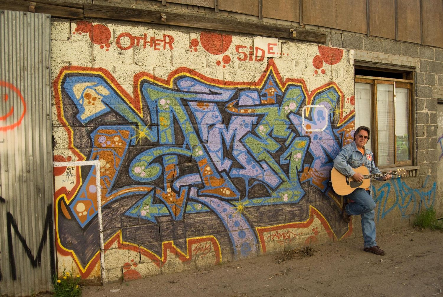 Colorful graffiti art adorns a concrete wall with musical performers playing guitar and instruments.