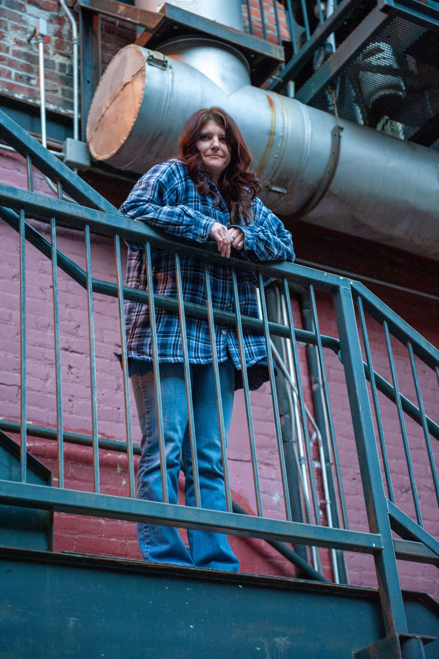 Person in casual wear leans on industrial metal railings overlooking a building interior.