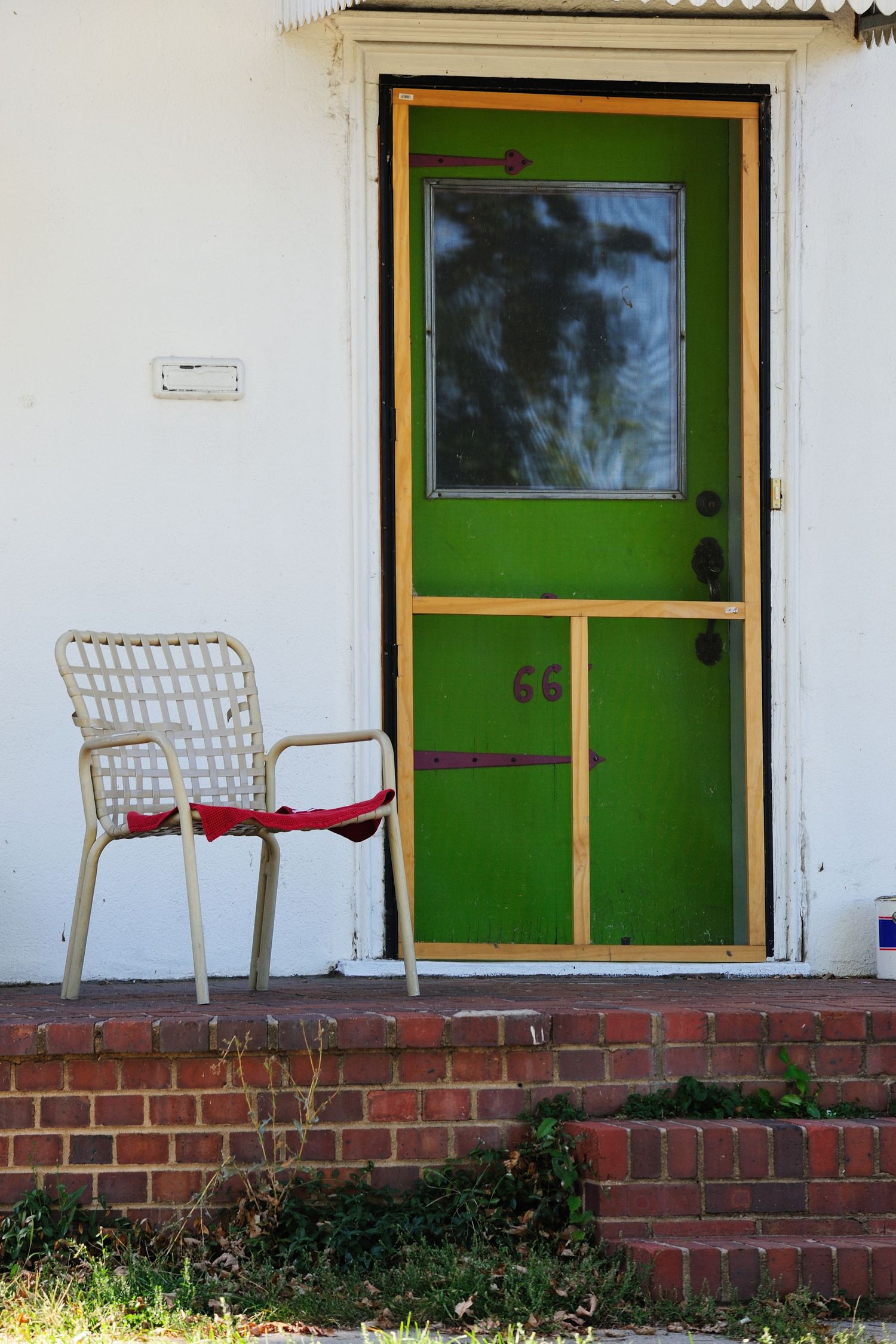 White porch with green door and two white chairs on brick foundation.