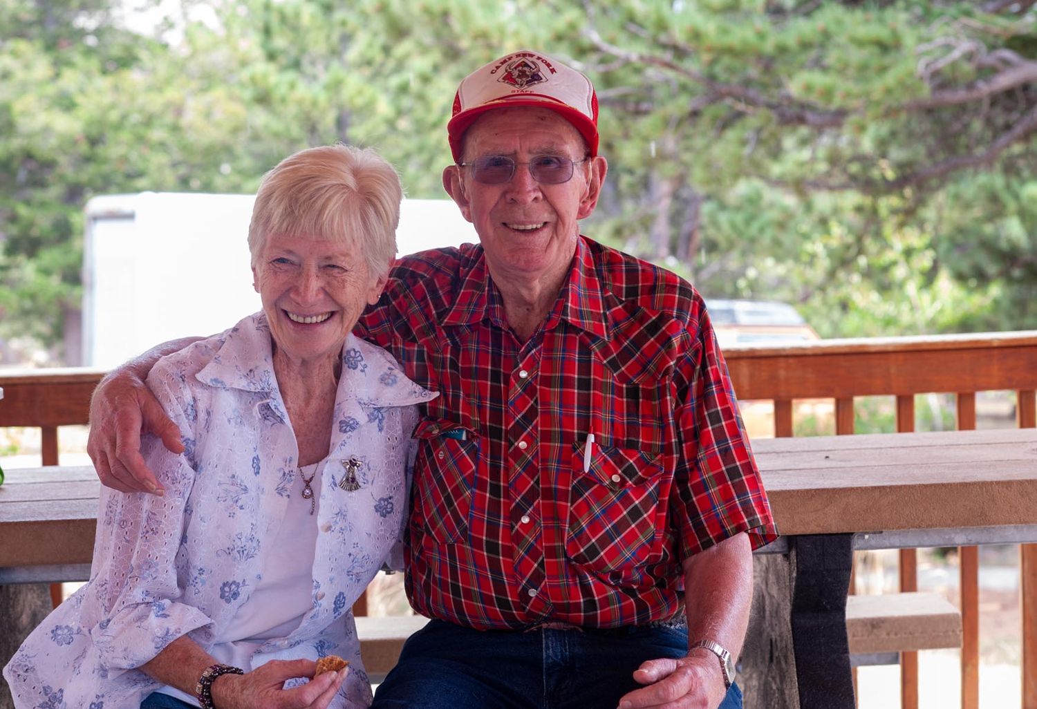 Elderly couple sitting together on an outdoor bench in casual attire.