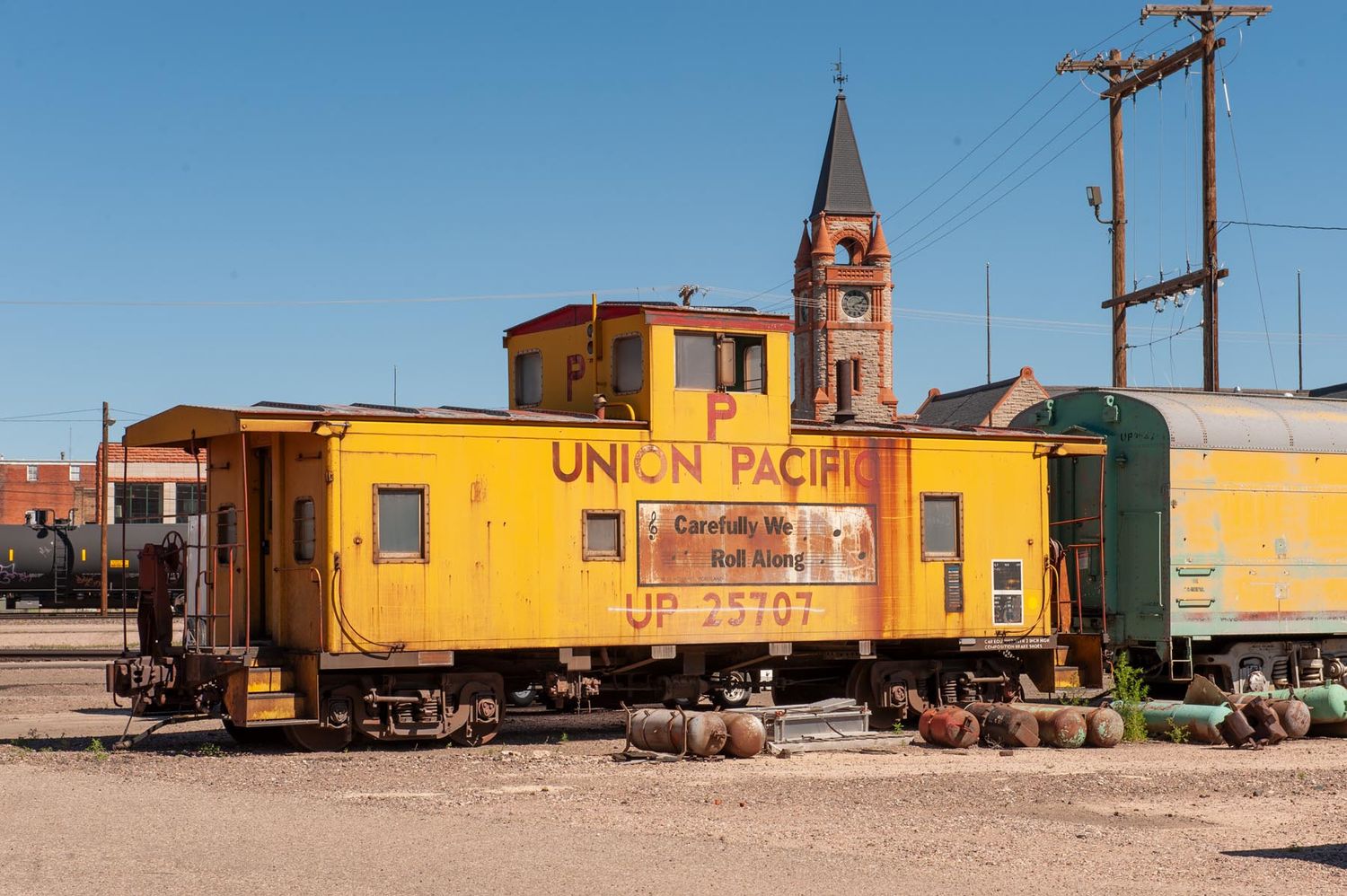 Yellow Union Pacific caboose parked on tracks with a church steeple visible in the background.