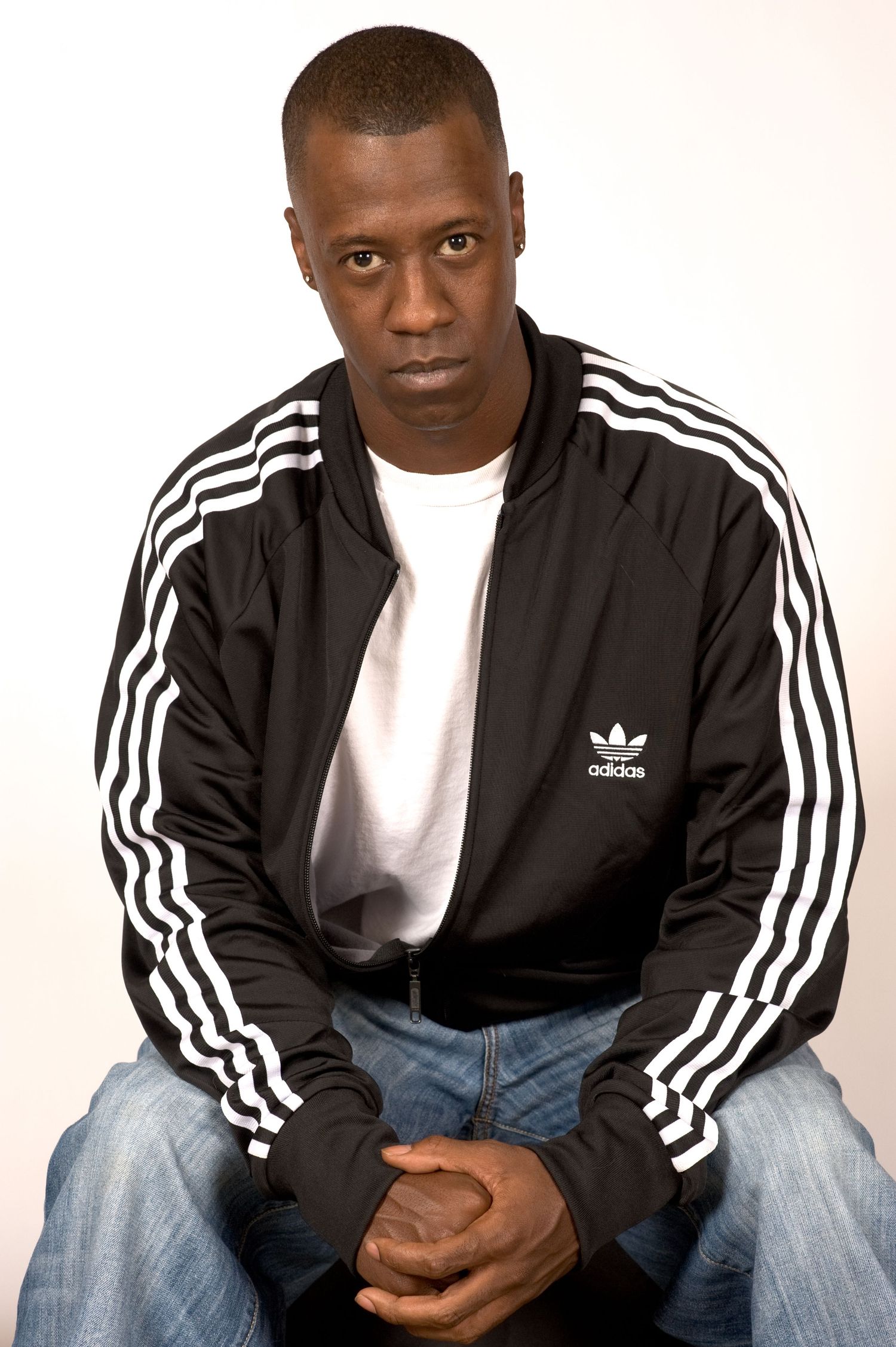 Portrait in Adidas track jacket and white t-shirt against light background.