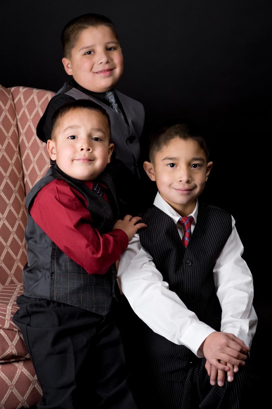 Two young boys in formal vests and dress clothes against dark background.