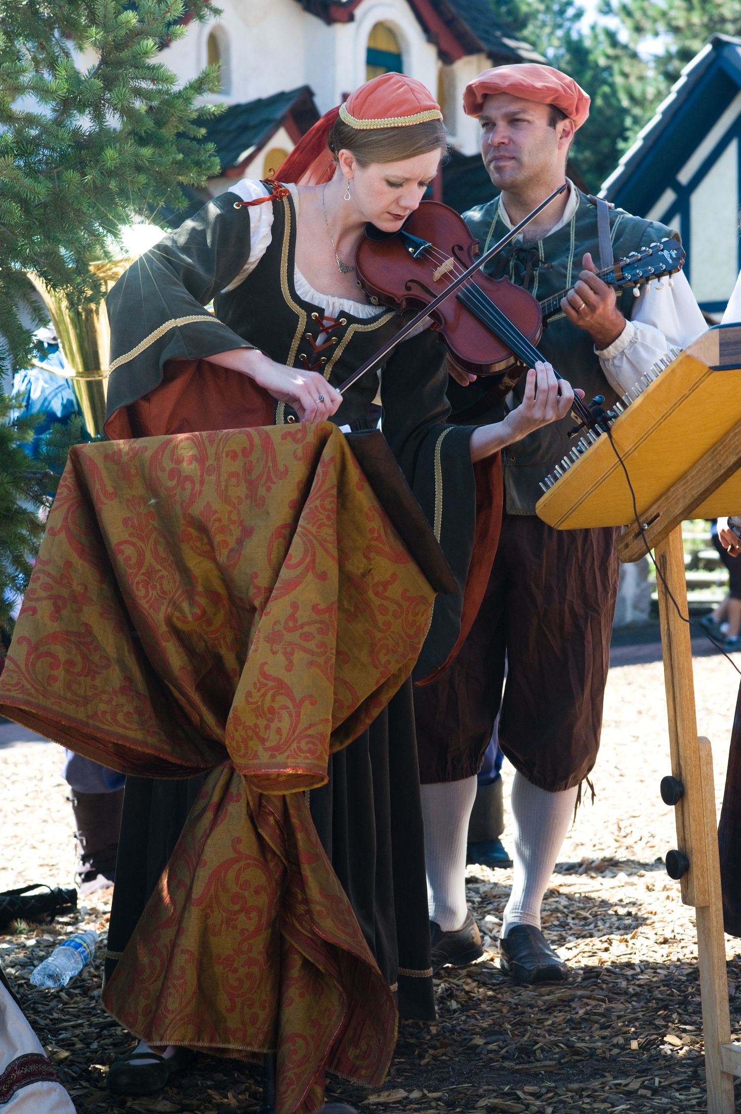 Musicians in period costumes perform with string instruments at a Renaissance fair.