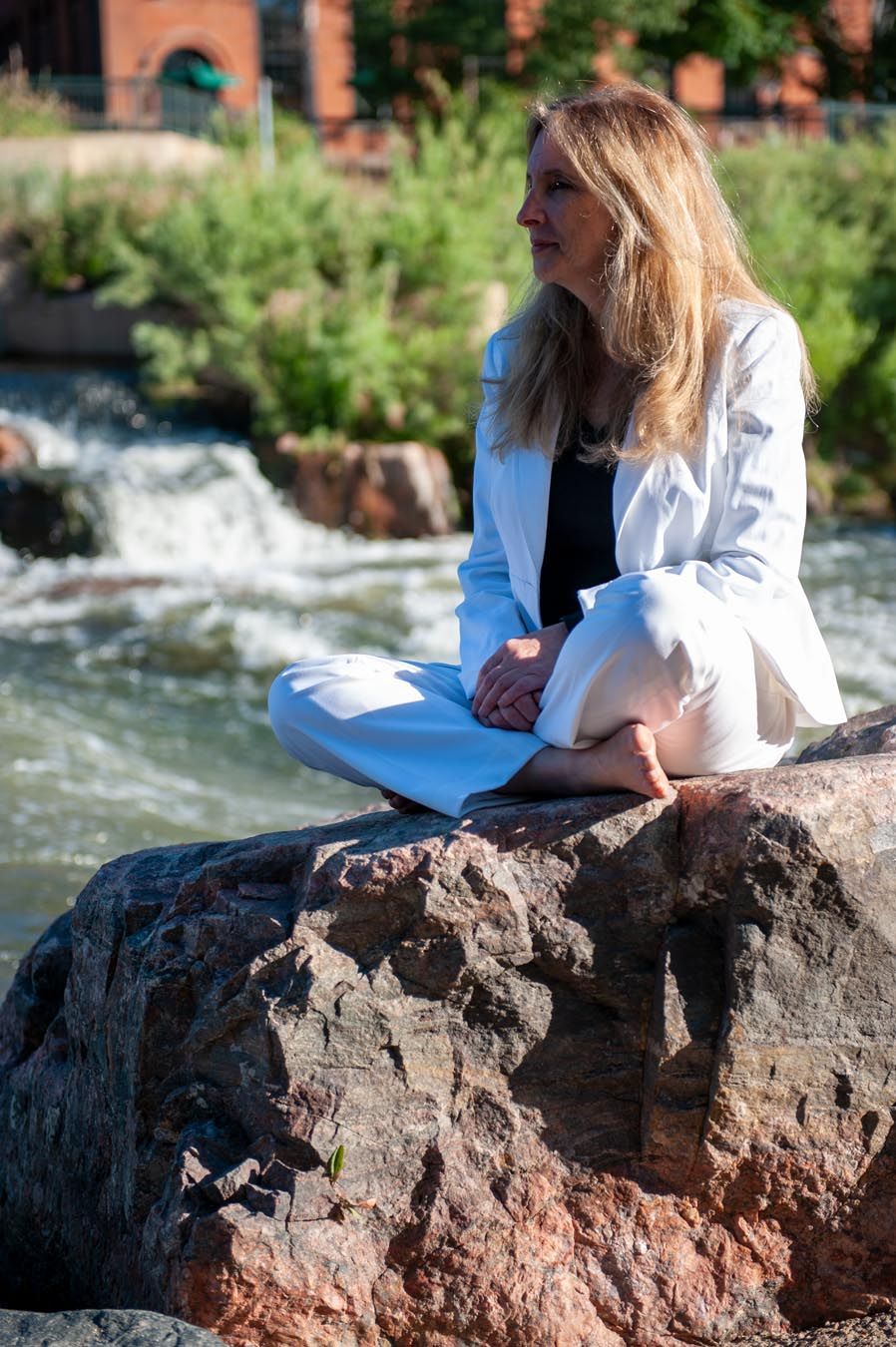Person sitting on rocky outcrop by rushing river with notebook.