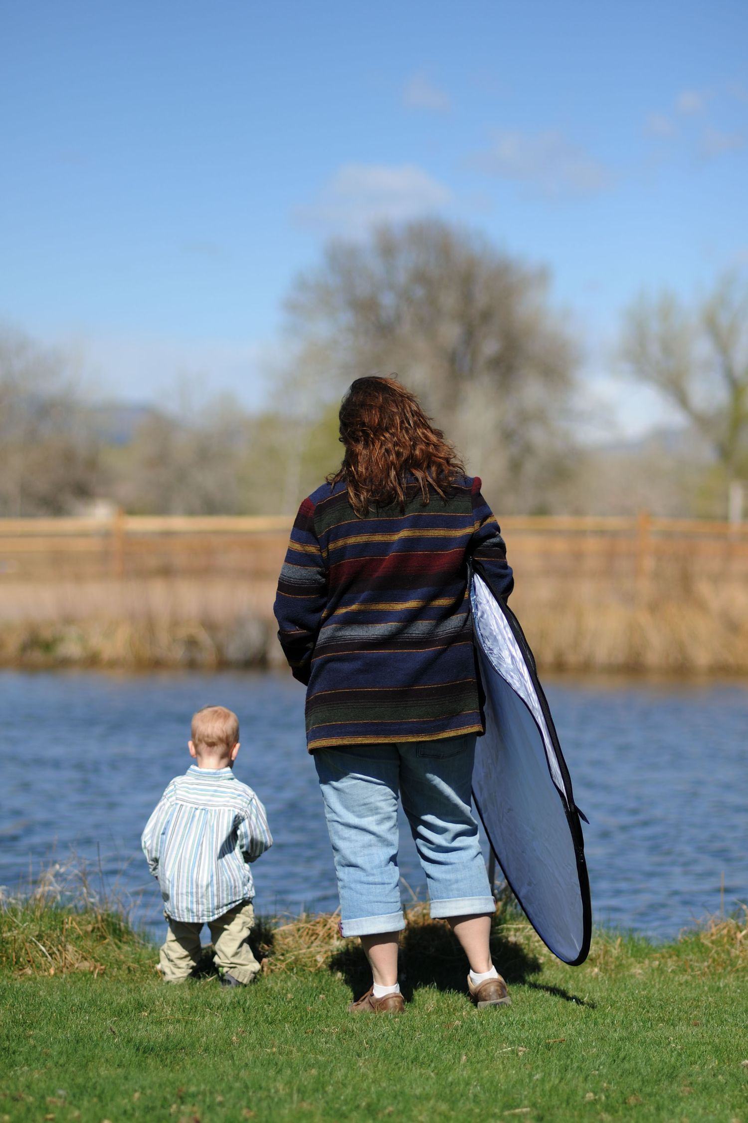 Parent and child sitting together by a lake on a sunny day watching the water.