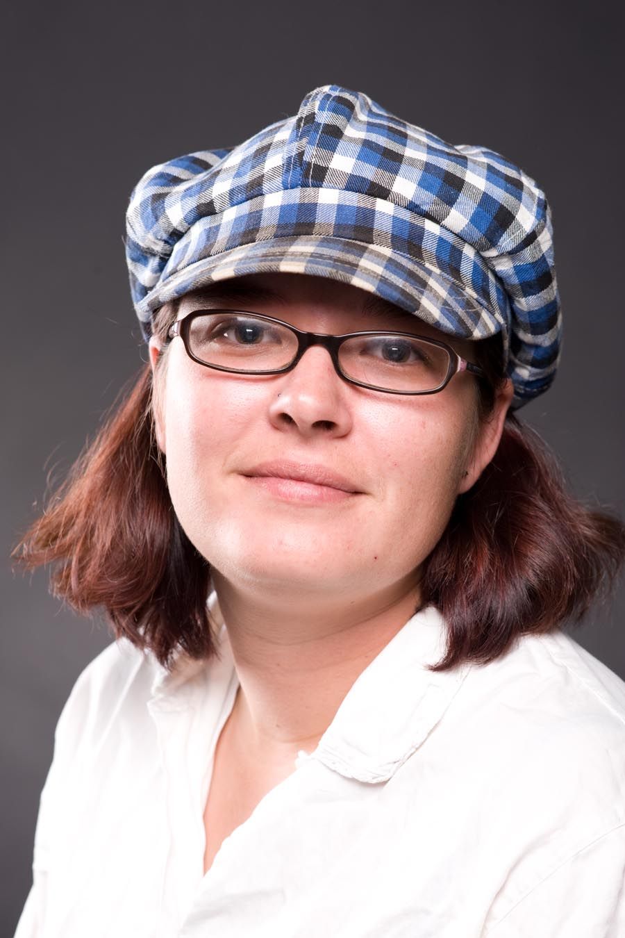 Portrait of person wearing plaid cap, glasses and white polo shirt against dark background.