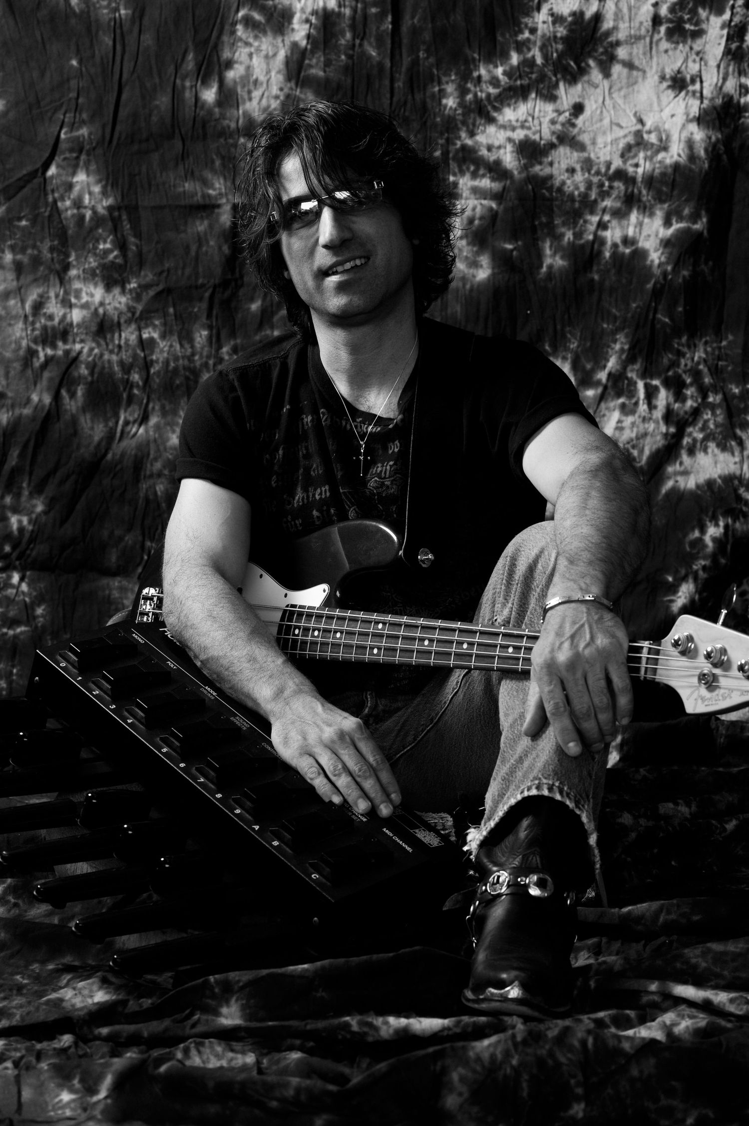 Black and white photo of a musician sitting with a bass guitar against a textured backdrop.