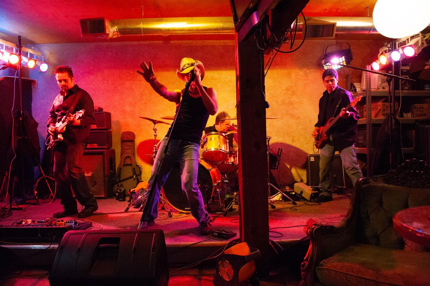 A rock band performs on stage with vibrant red lighting creating an energetic atmosphere during a live concert performance.